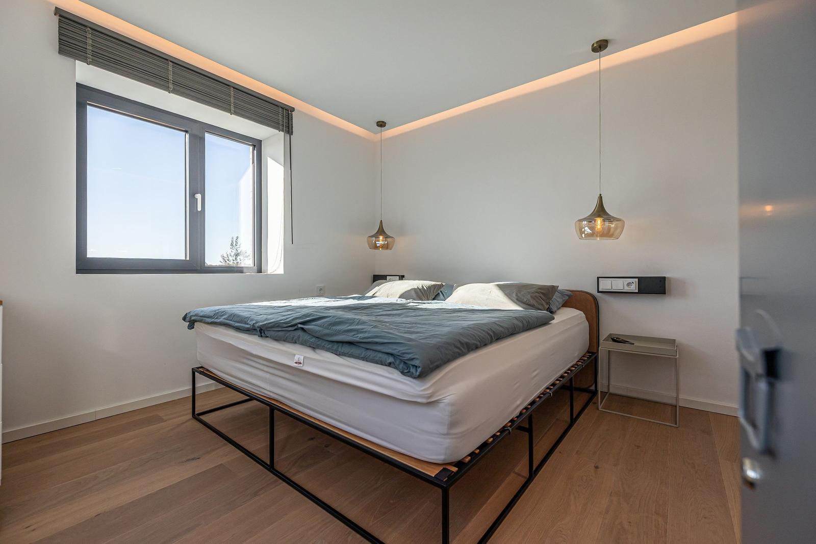 Schlafzimmer mit Bett, Fenster und zwei Hängelampen.