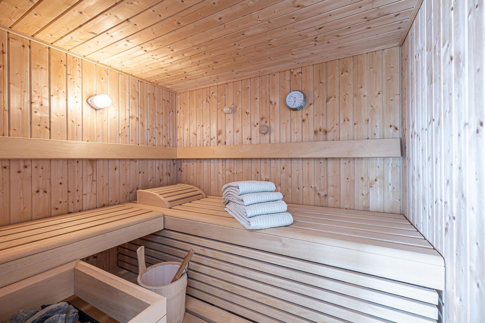 Sauna mit Holzbank, Handtuchstapel und Thermometer an der Wand.