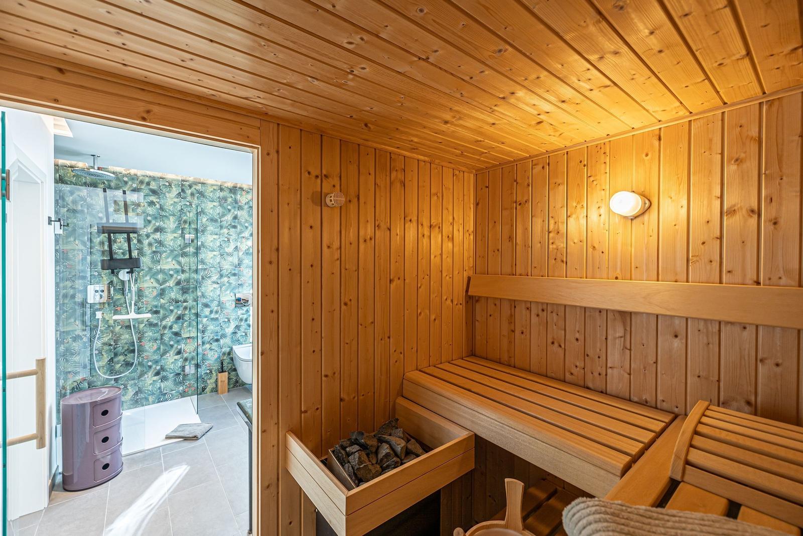 Sauna mit Holzbank und Holzwand. Durchgang zur Dusche mit Glaswand.