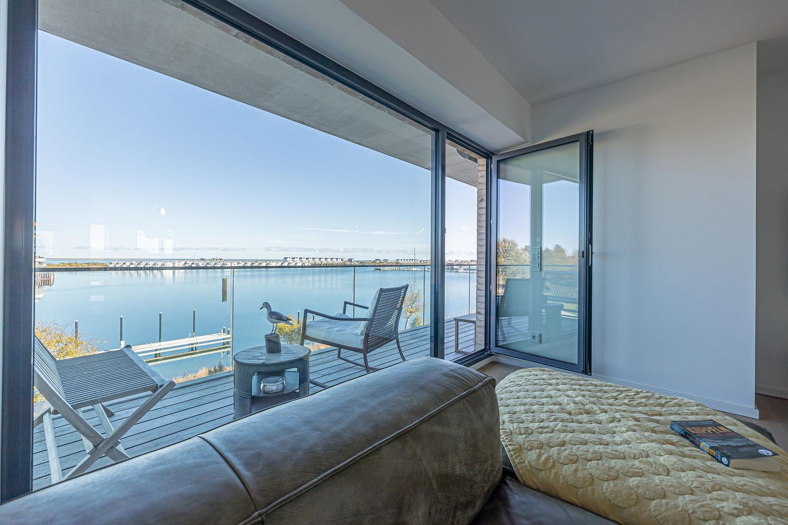Wohnbereich mit Blick auf Wasser und Terrasse mit Sitzmöbeln.