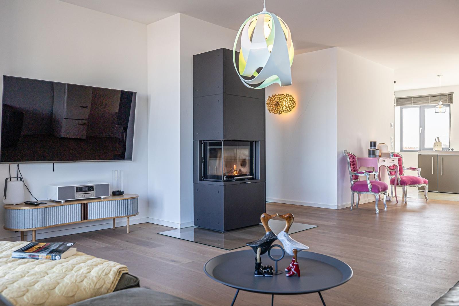 Wohnbereich mit Kamin, Fernseher und pinkem Sitzbereich.