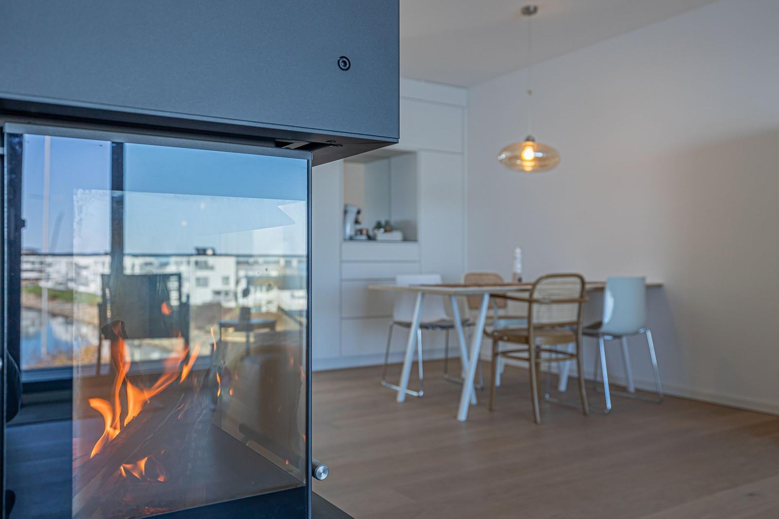 Kamin mit Flamme im Vordergrund, dahinter Essbereich mit Tisch und Stühlen.