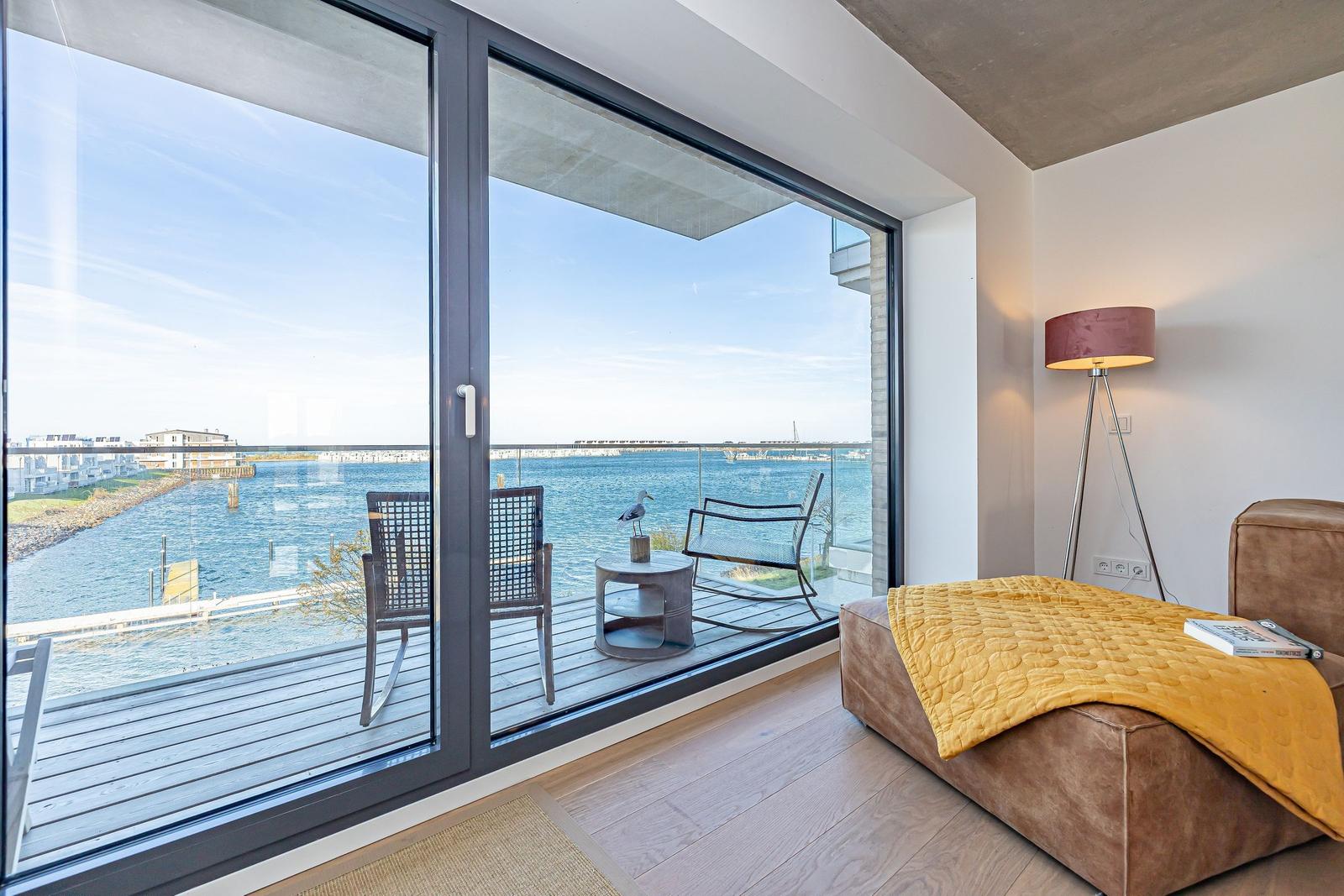 Zimmer mit Balkon und Blick auf Wasser. Gelber Deckenbezug auf Sofa.