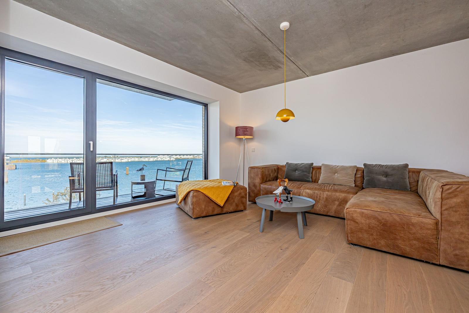 Wohnzimmer mit Blick auf Wasser, braunes Sofa und Holzboden.