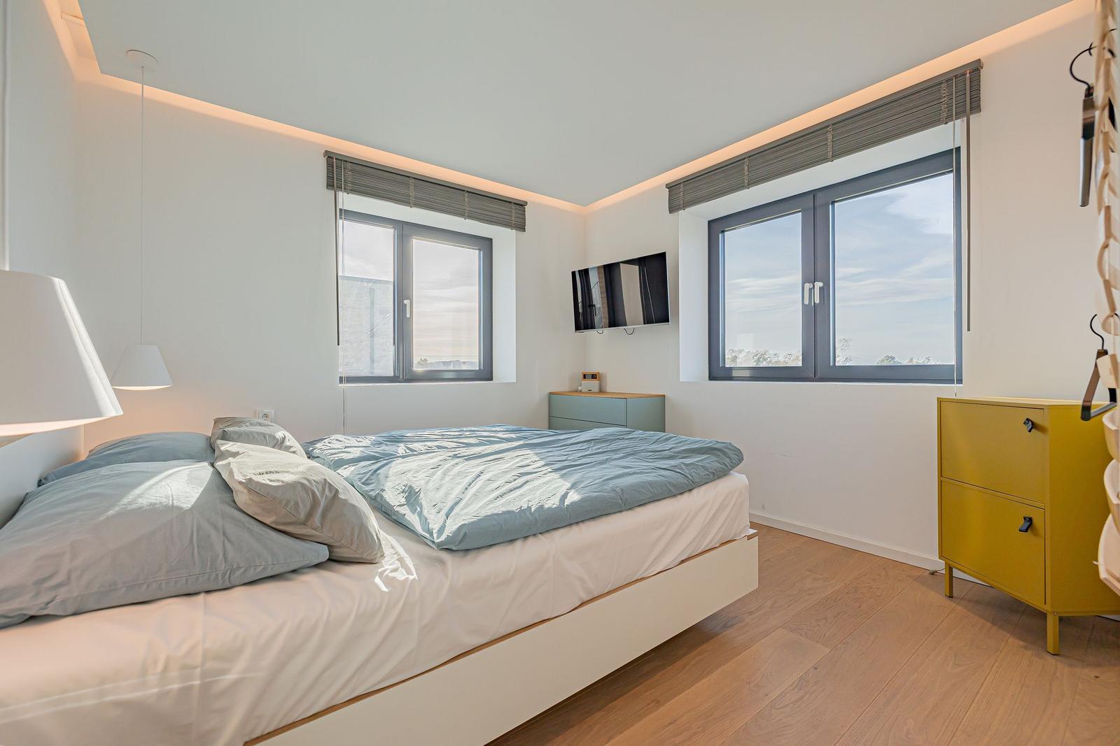 Schlafzimmer mit Bett, Fenstern und gelbem Schrank.