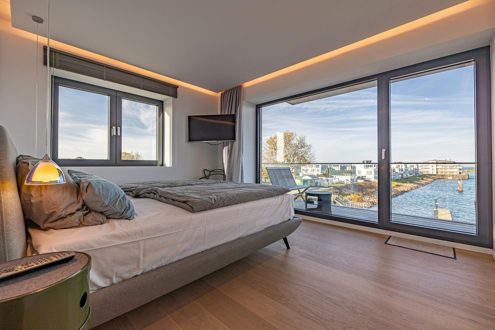 Schlafzimmer mit großem Bett und Blick auf Wasser und Balkon.