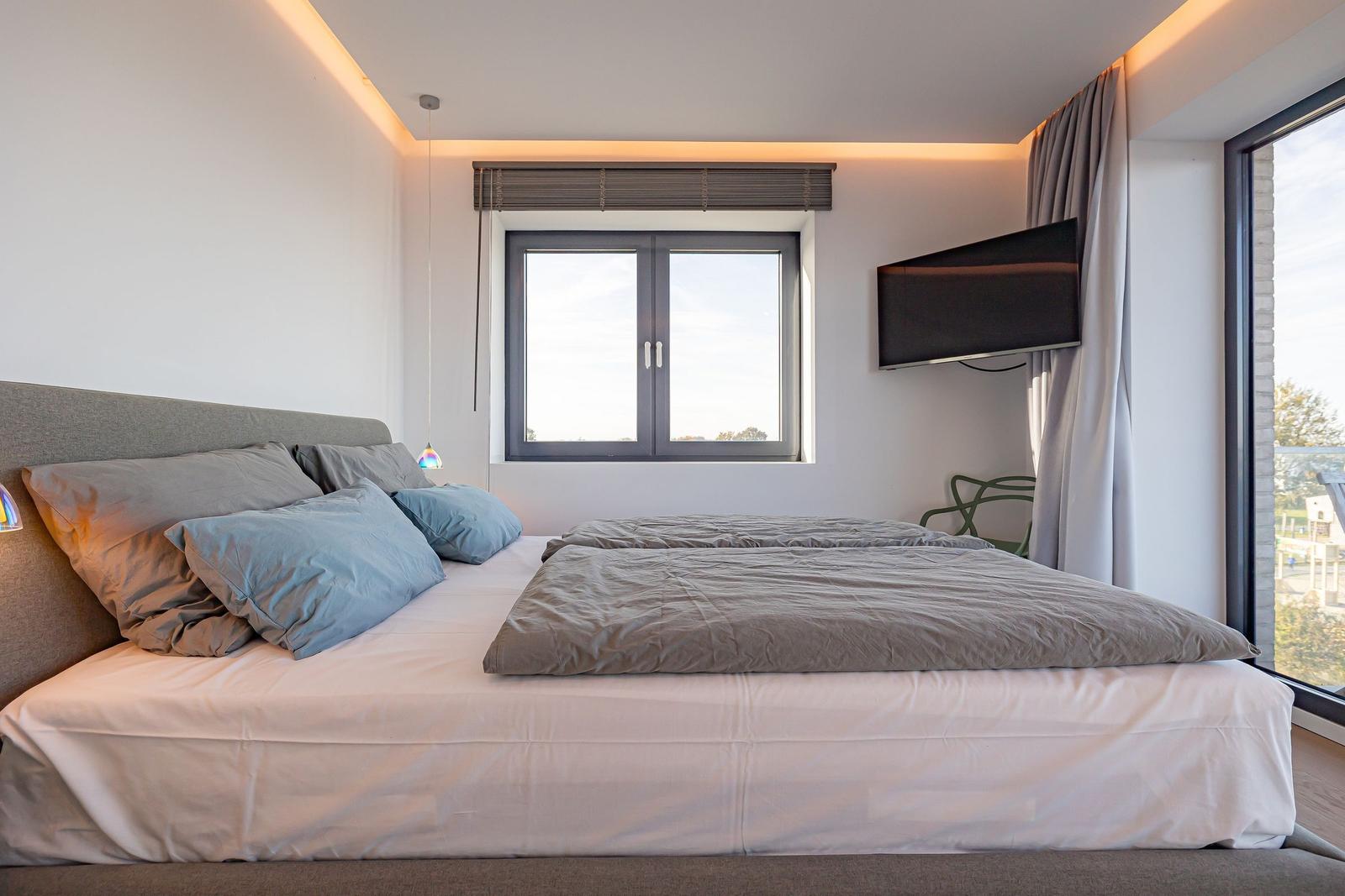 Schlafzimmer mit Doppelbett, Fenster und Wandfernseher.