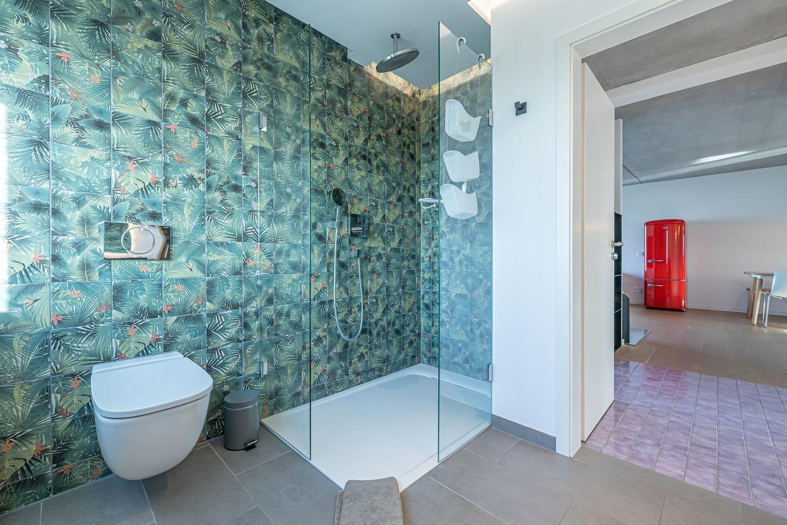 Bad mit Dusche und tropischen Fliesen. Roter Kühlschrank im angrenzenden Raum.