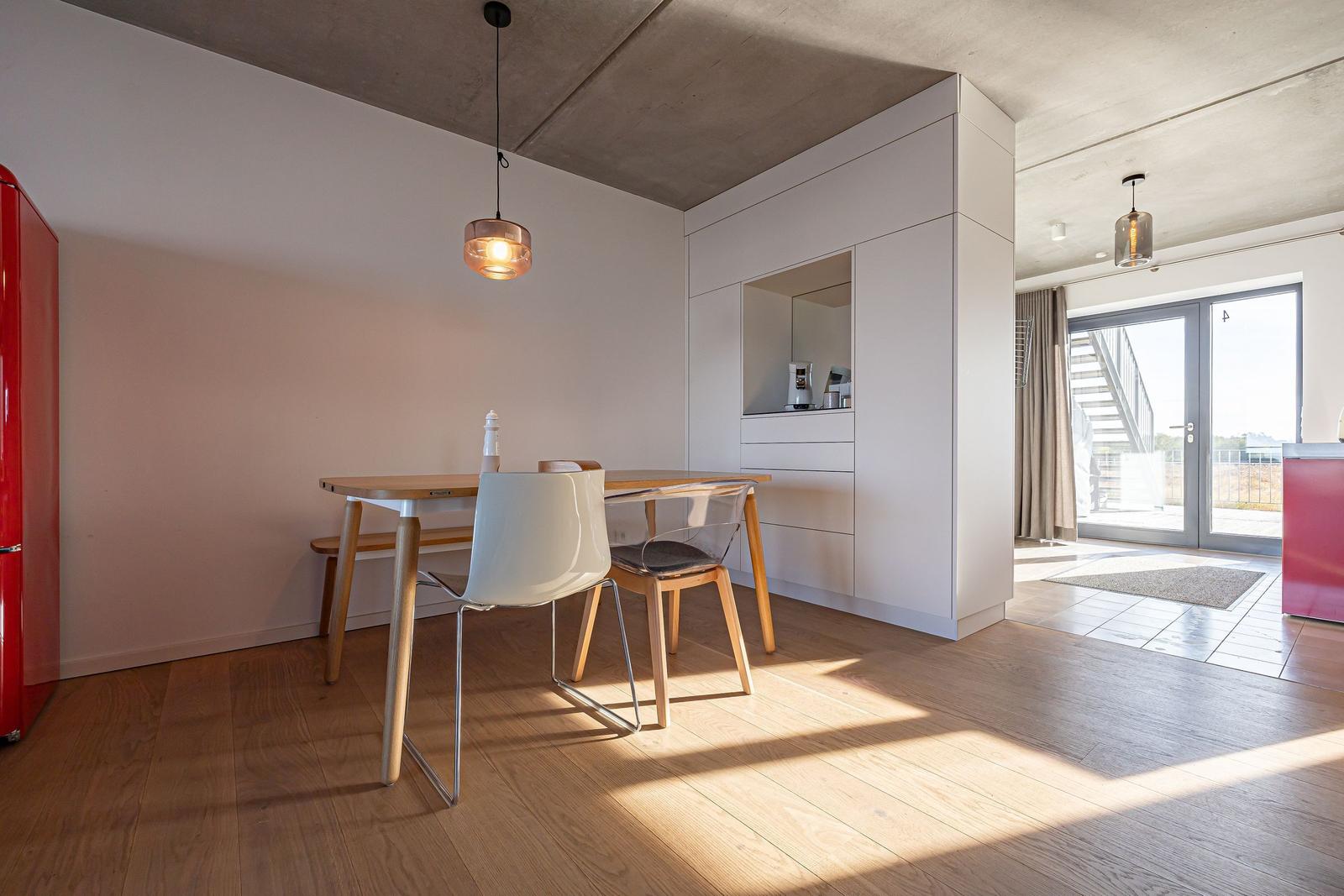 Essbereich mit Tisch, Stühlen und rotem Kühlschrank. Durchgang zur Terrasse mit Glasfront.