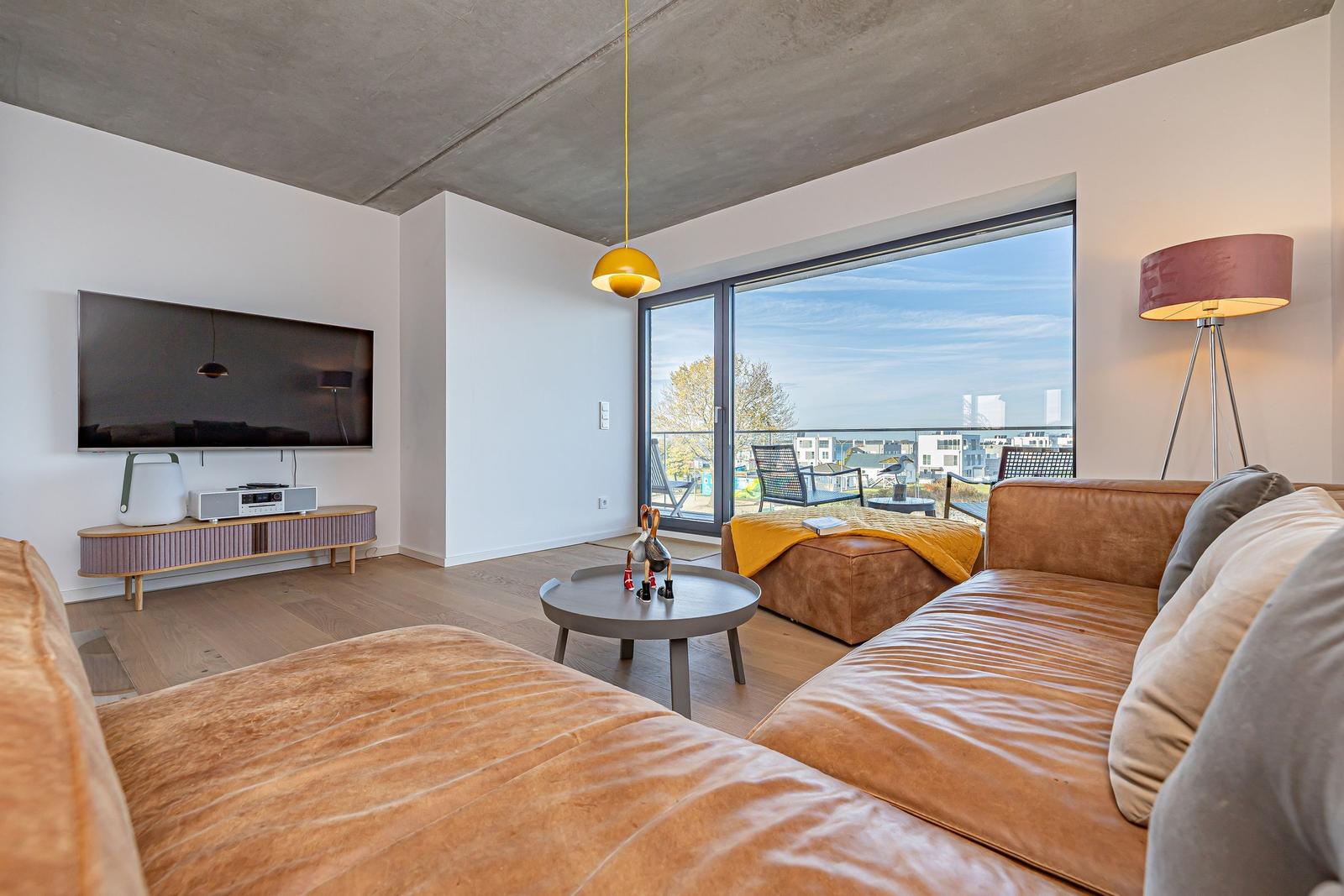 Wohnzimmer mit Ledersofa, Fernseher und Balkonblick.