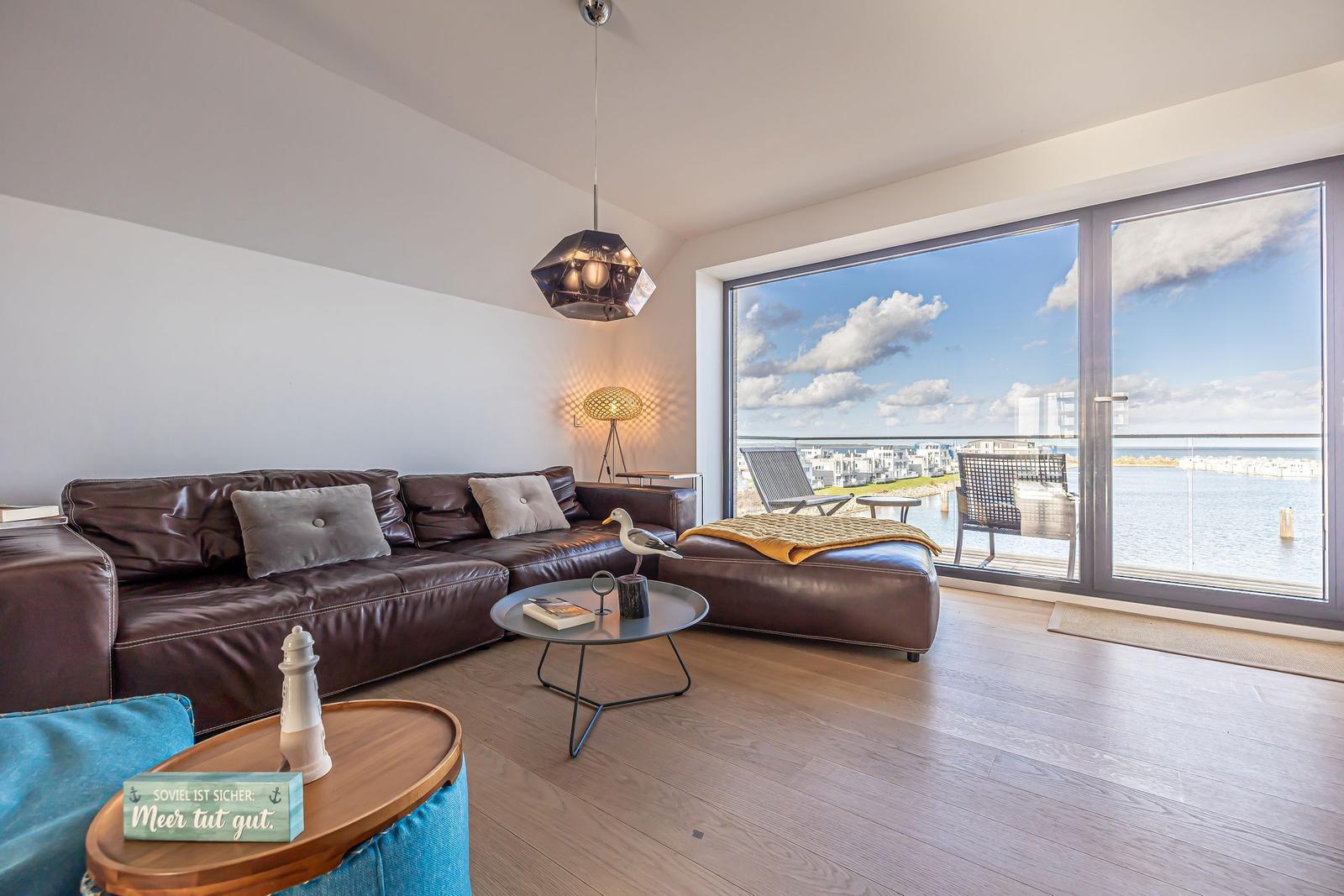 Wohnzimmer mit braunem Sofa und Balkonblick auf Wasser.