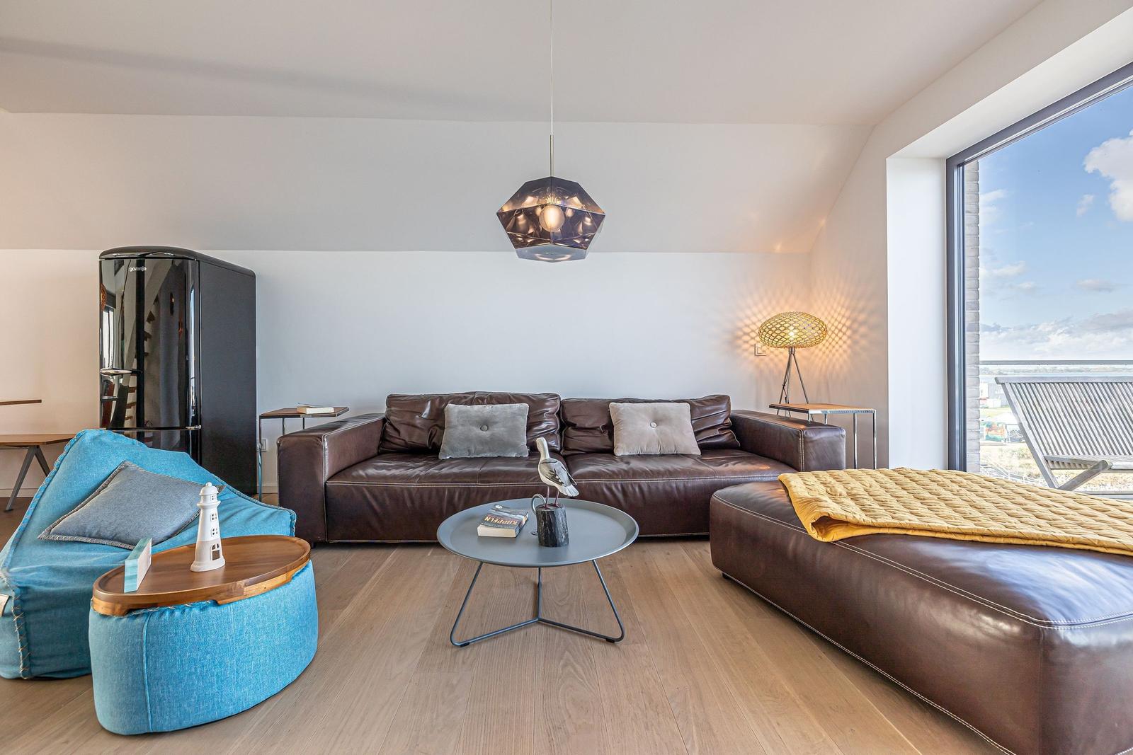 Wohnzimmer mit Ledersofa, blauem Sitzkissen und Blick auf Balkon