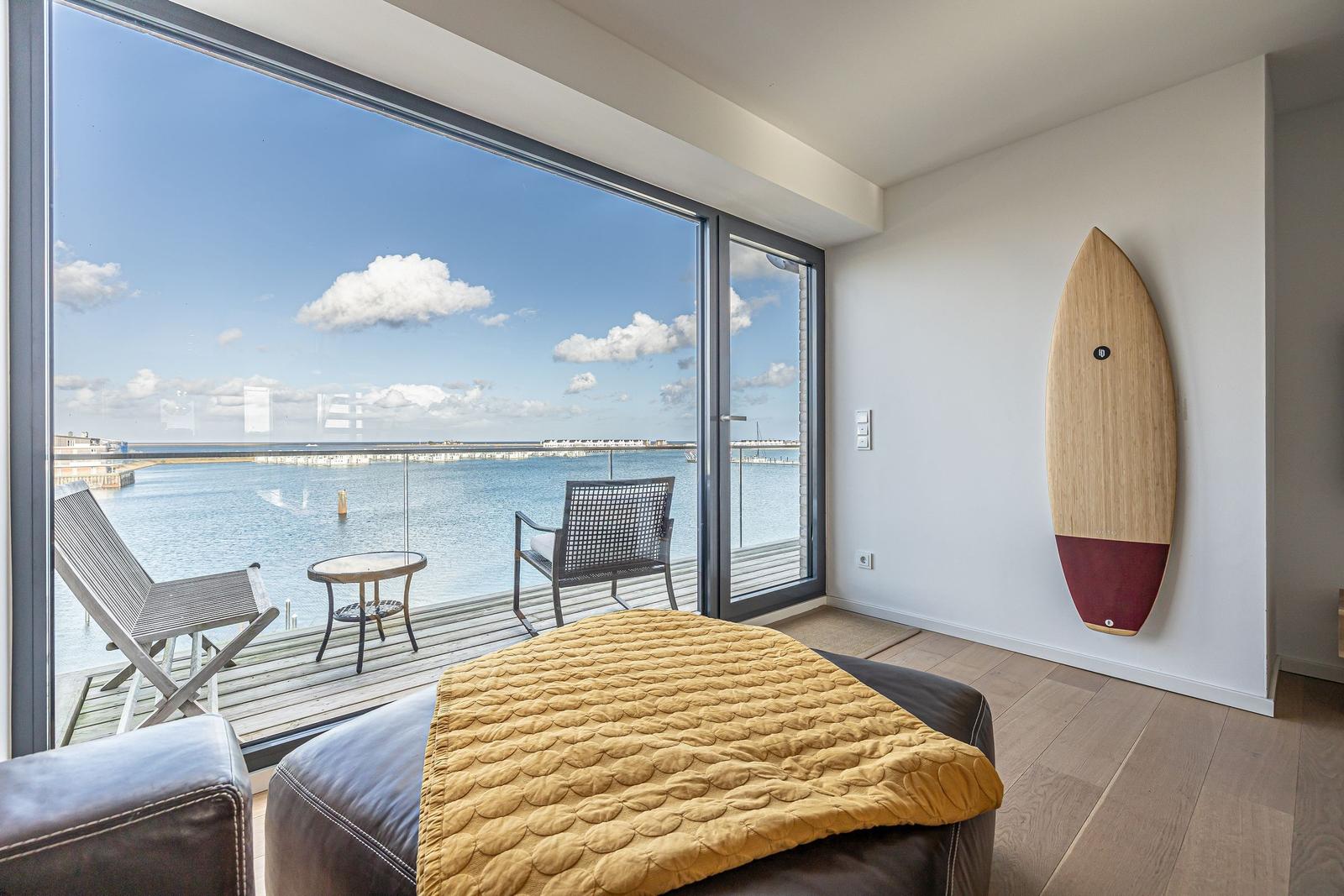 Raum mit Blick auf Wasser, Balkon mit Stühlen und Tisch, Surfbrett an Wand