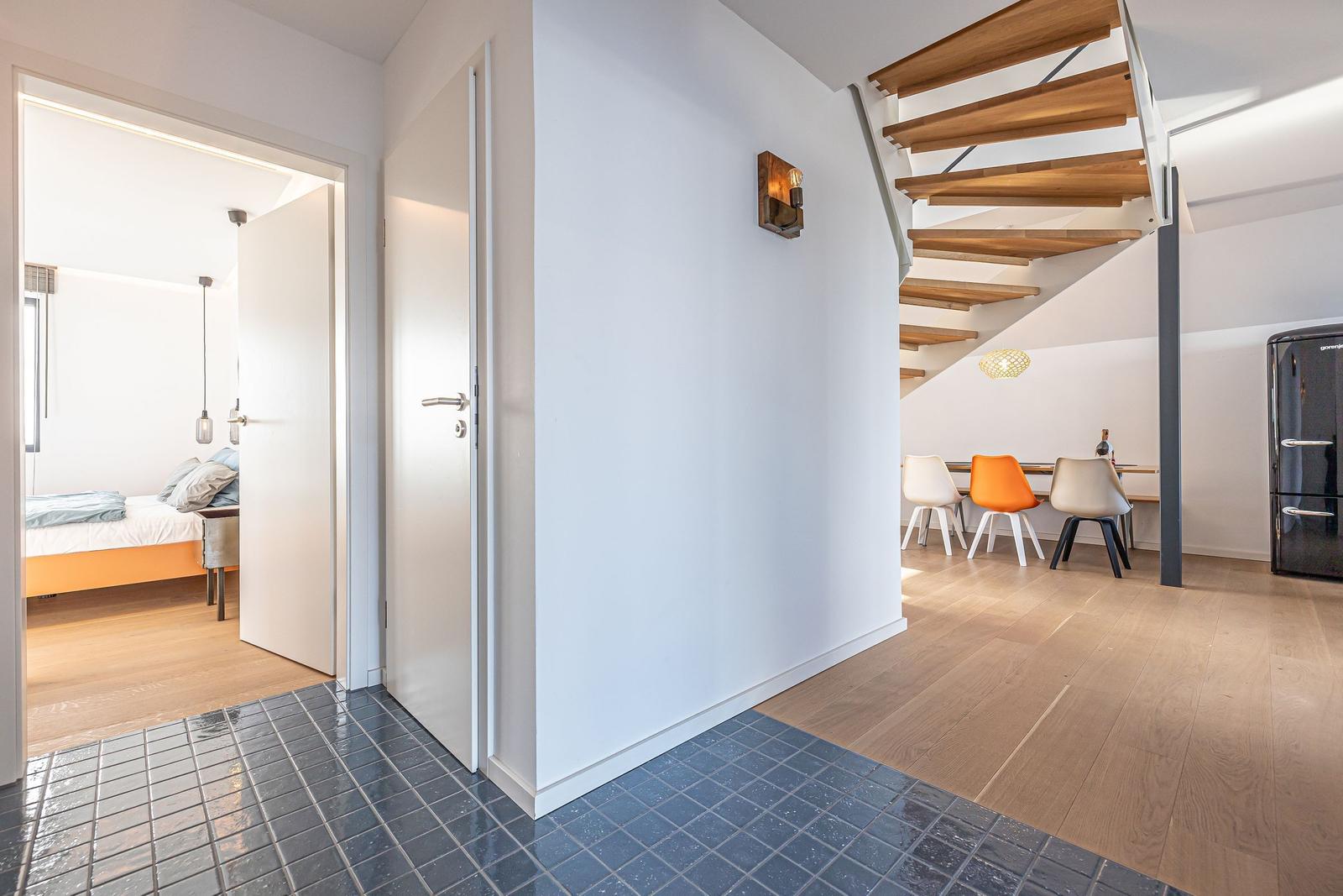 Eingangsbereich mit Treppenhaus, Schlafzimmer und Essbereich mit orangefarbener Stuhle.