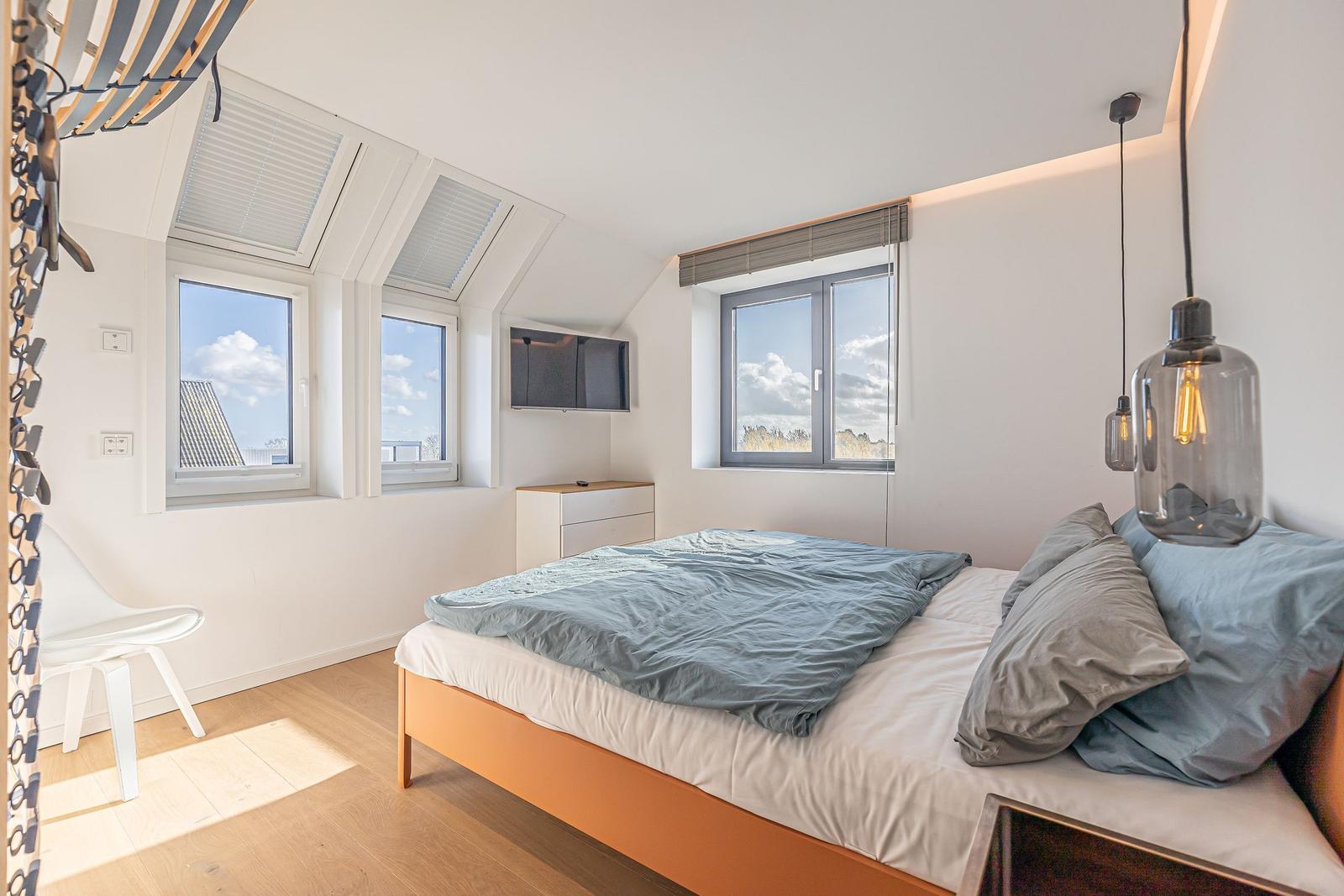 Schlafzimmer mit Dachfenstern, Bett und Fernseher.