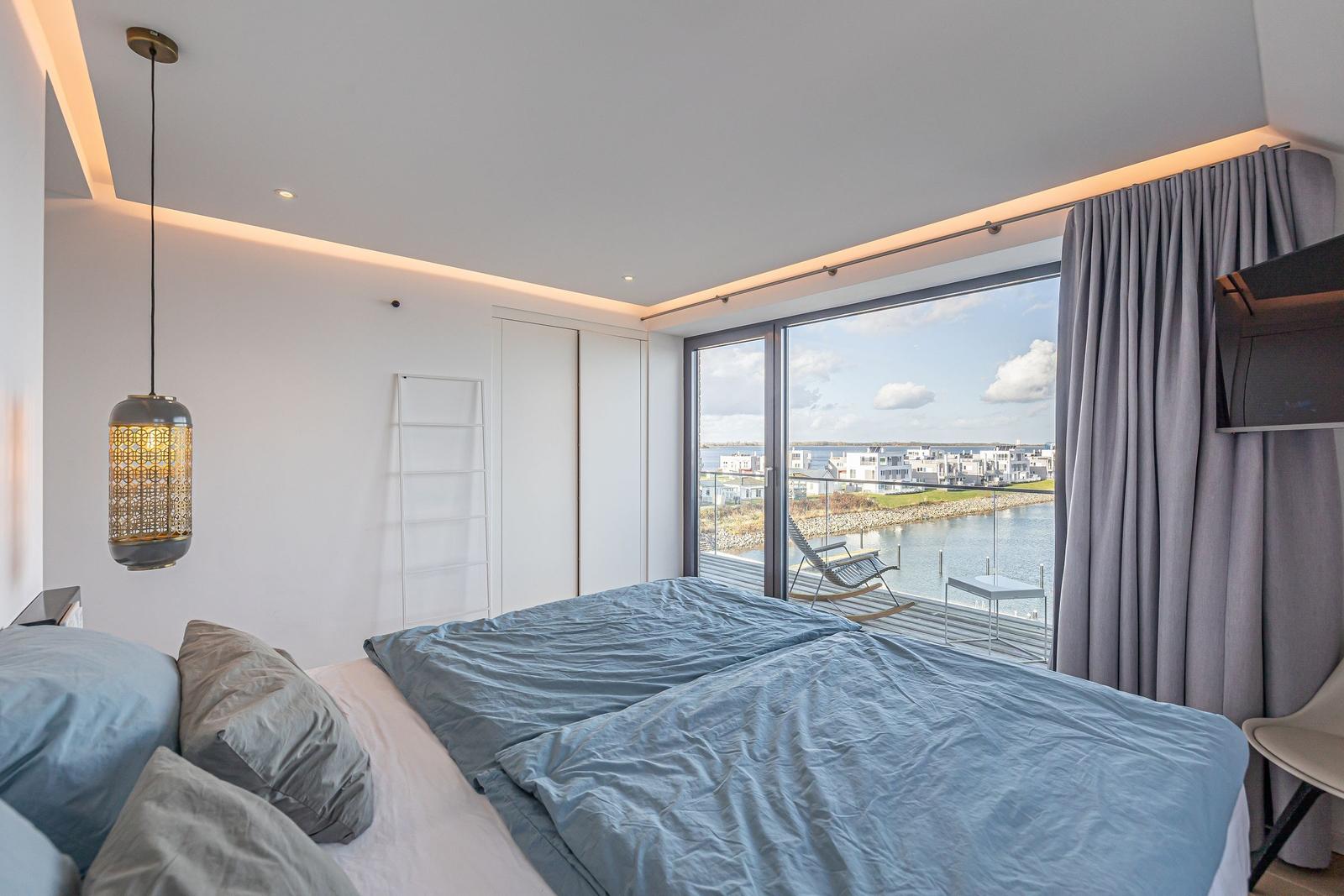 Schlafzimmer mit Blick auf Wasser und Terrasse mit Liegestuhl.
