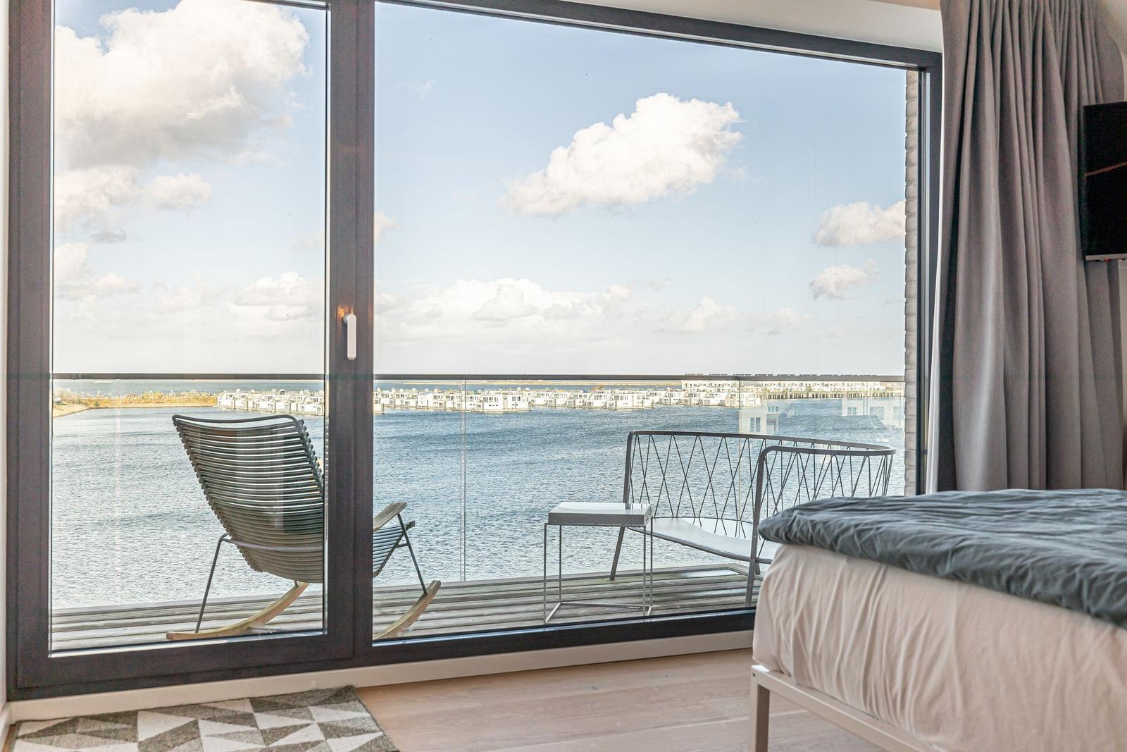 Schlafzimmer mit Blick auf Wasser und Terrasse mit Stuhl und Tisch.