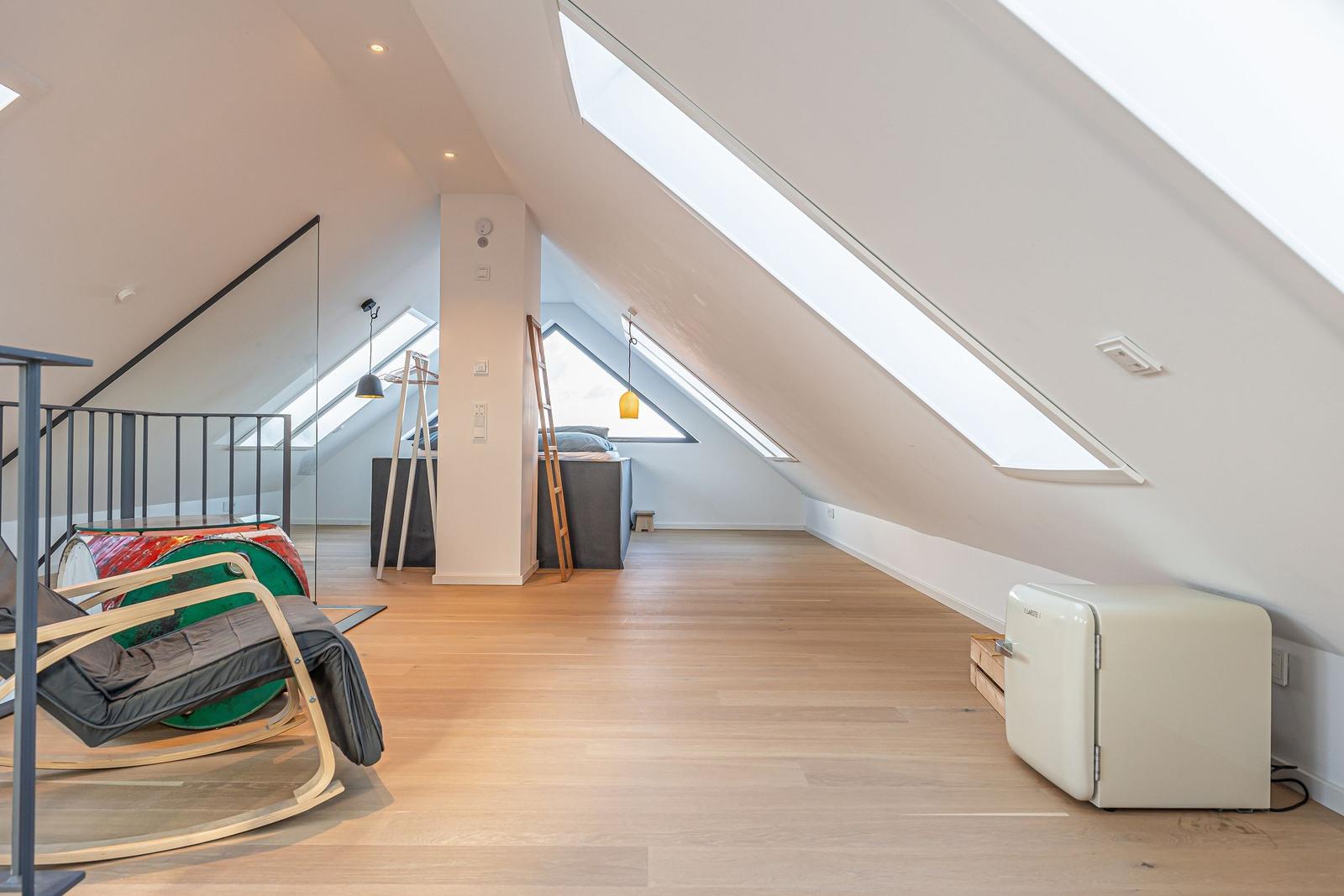 Dachgeschoss mit Holzboden, Dachschrägen, Dachfenstern und kleinem Kühlschrank.