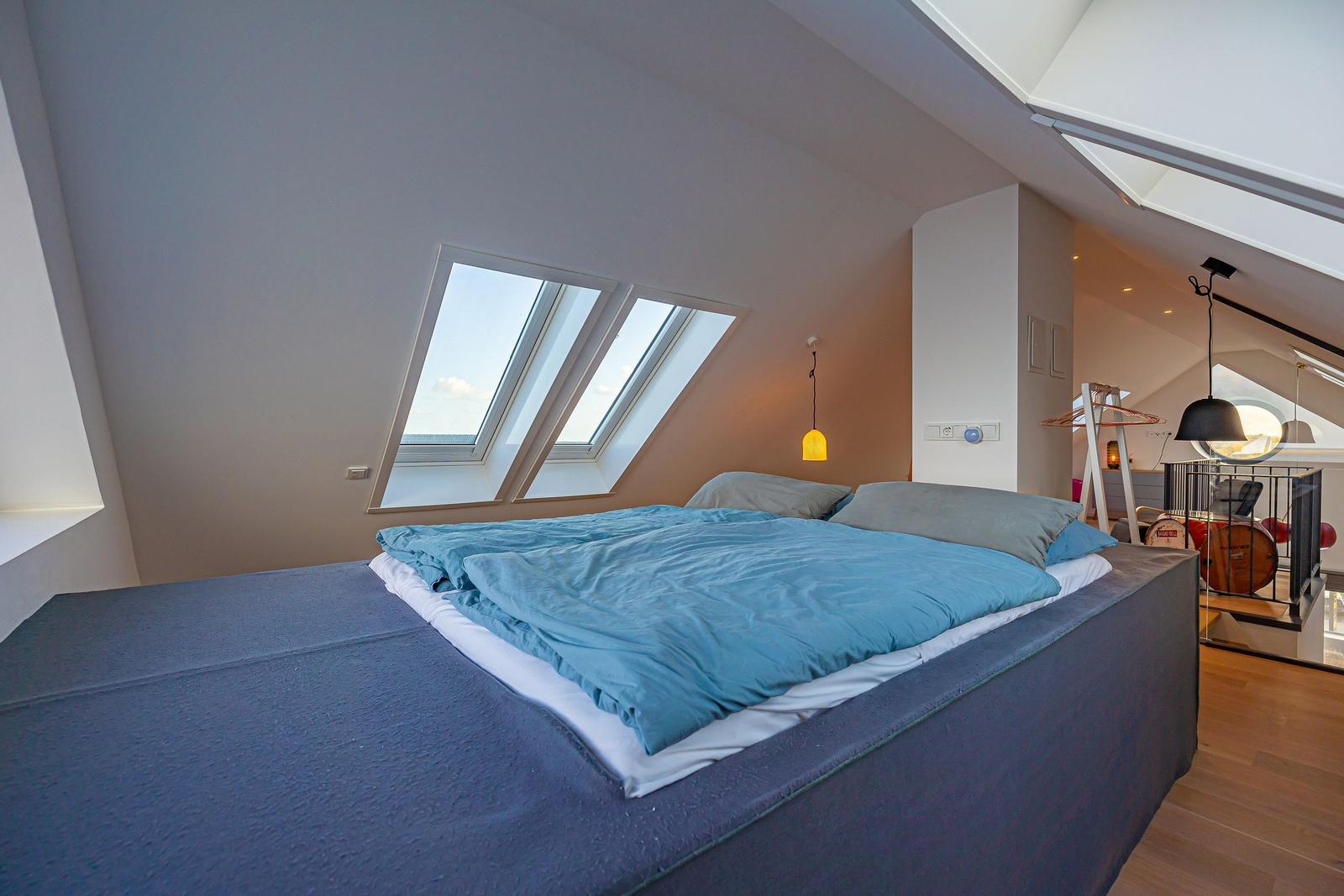 Schlafzimmer mit Dachschrägen, Dachfenster und Bett mit blauer Bettwäsche.
