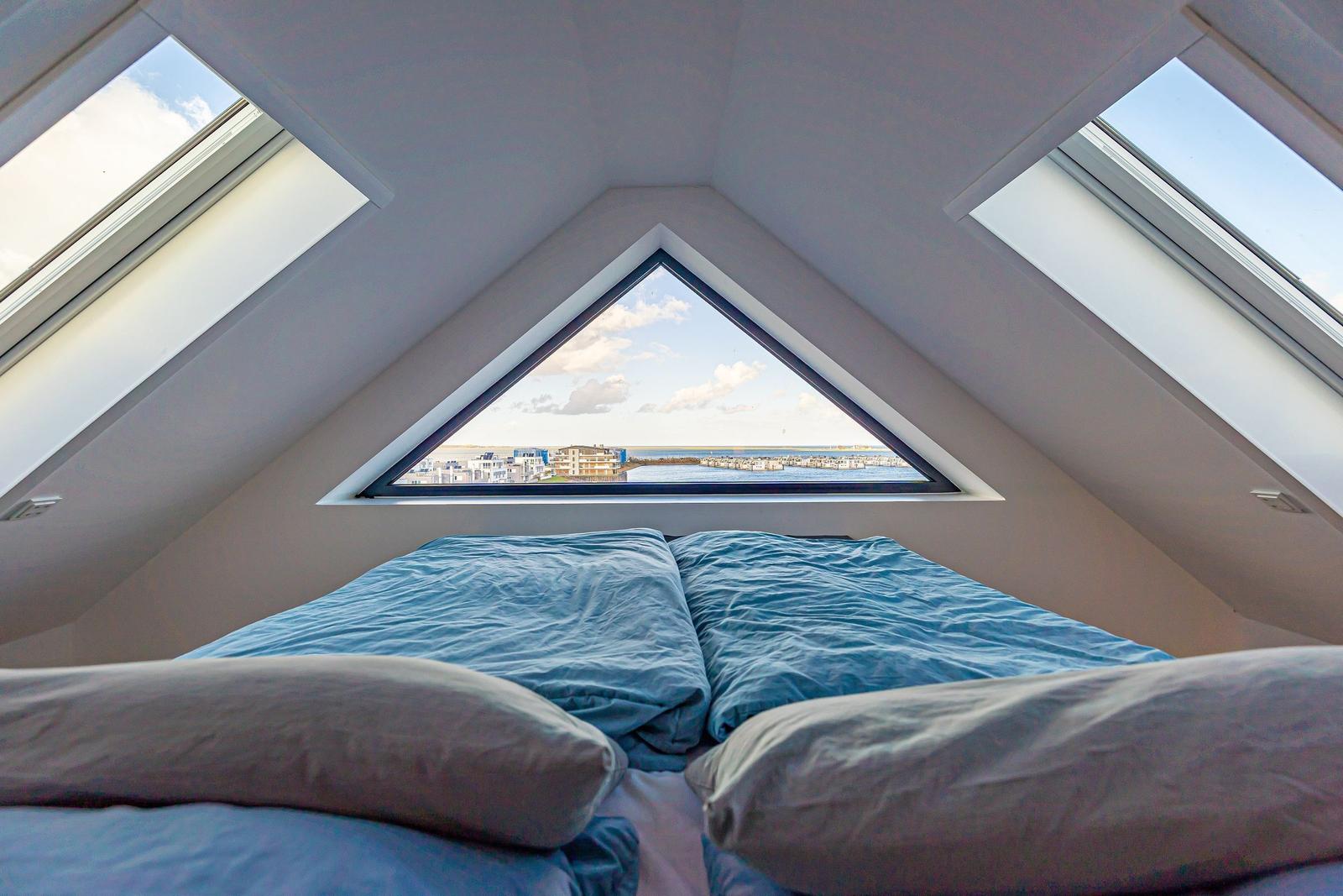 Schlafzimmer mit Dachfenstern und Blick auf Wasser und Gebäude.