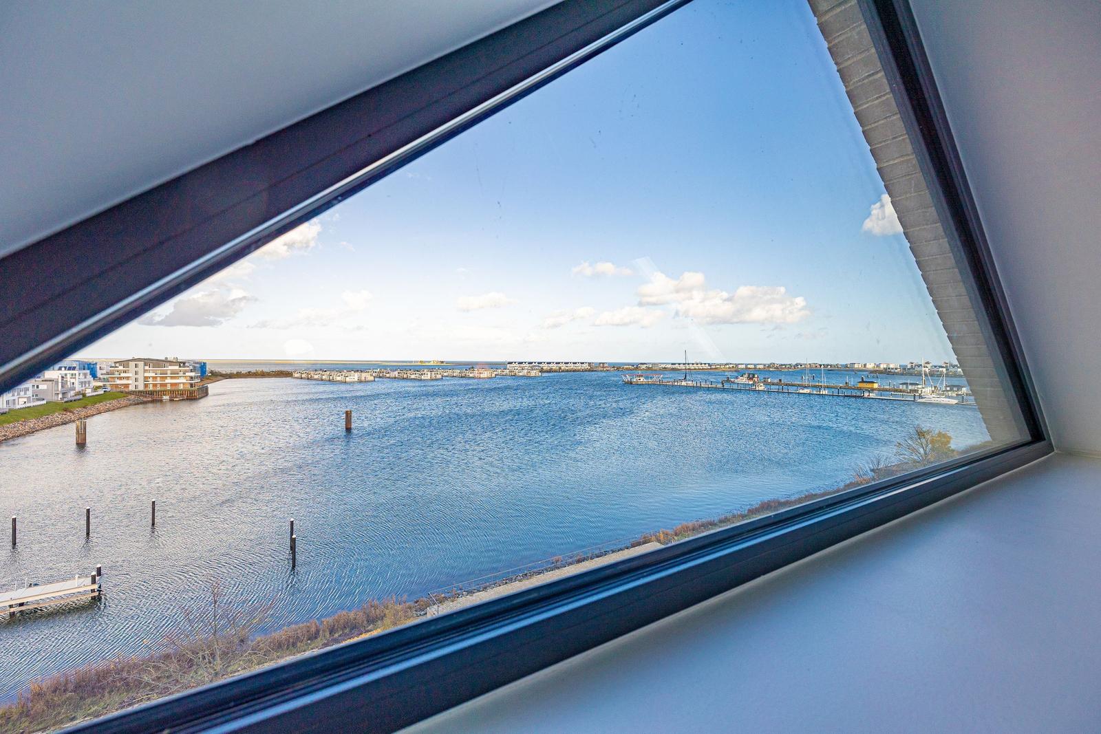 Aus dem Fenster sieht man einen Hafen mit Booten und einem blauen Himmel.