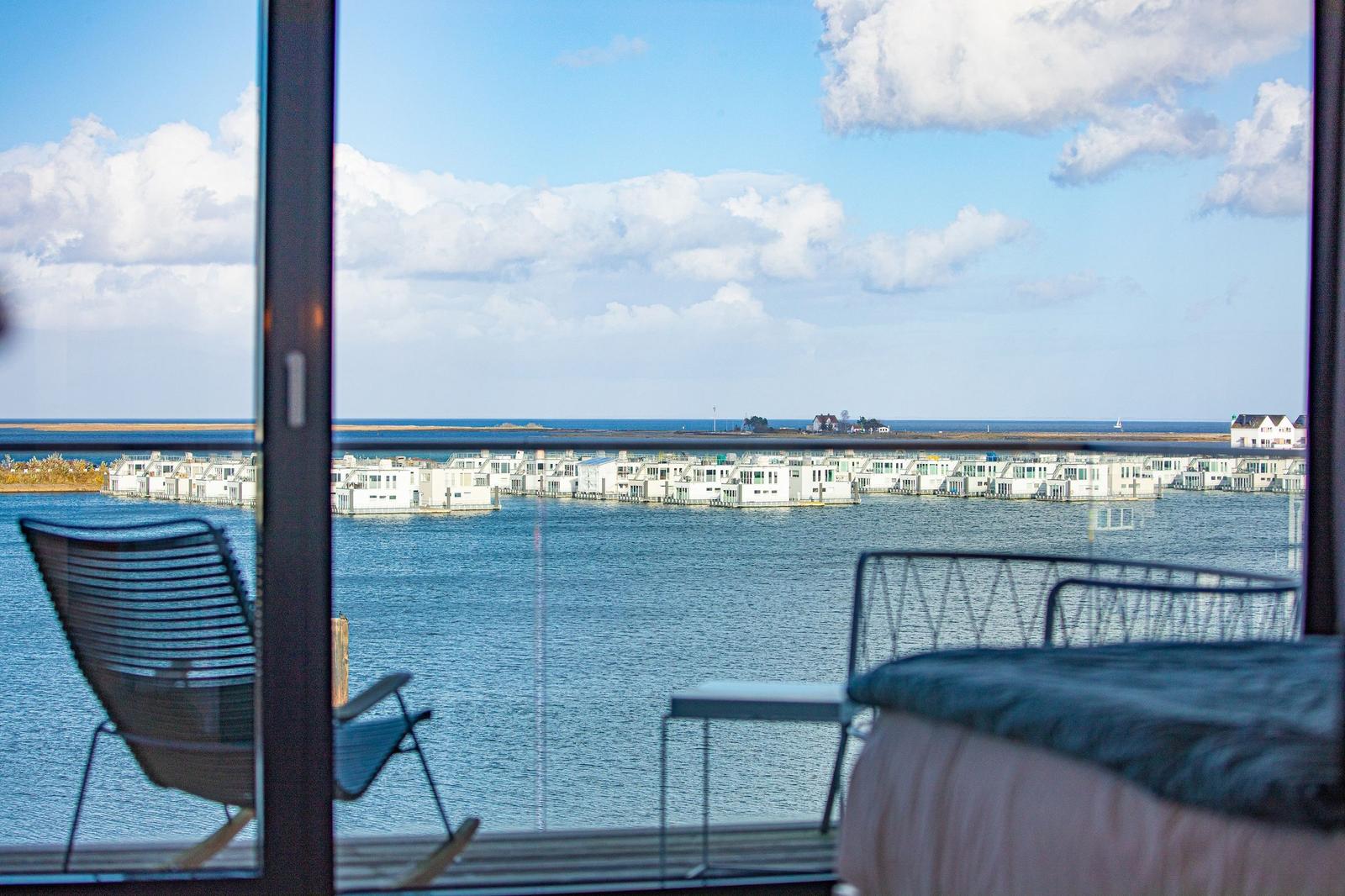 Blick auf Wasser und weiße Häuser vom Balkon mit Stuhl und Tisch.