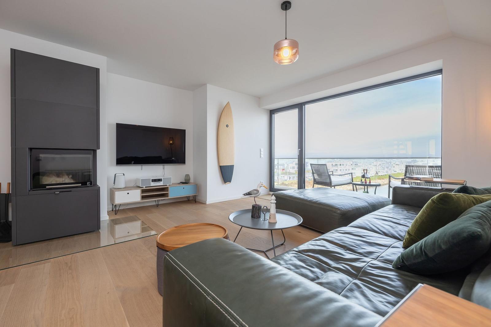 Wohnzimmer mit Sofa, Fernseher und Blick auf den Balkon.