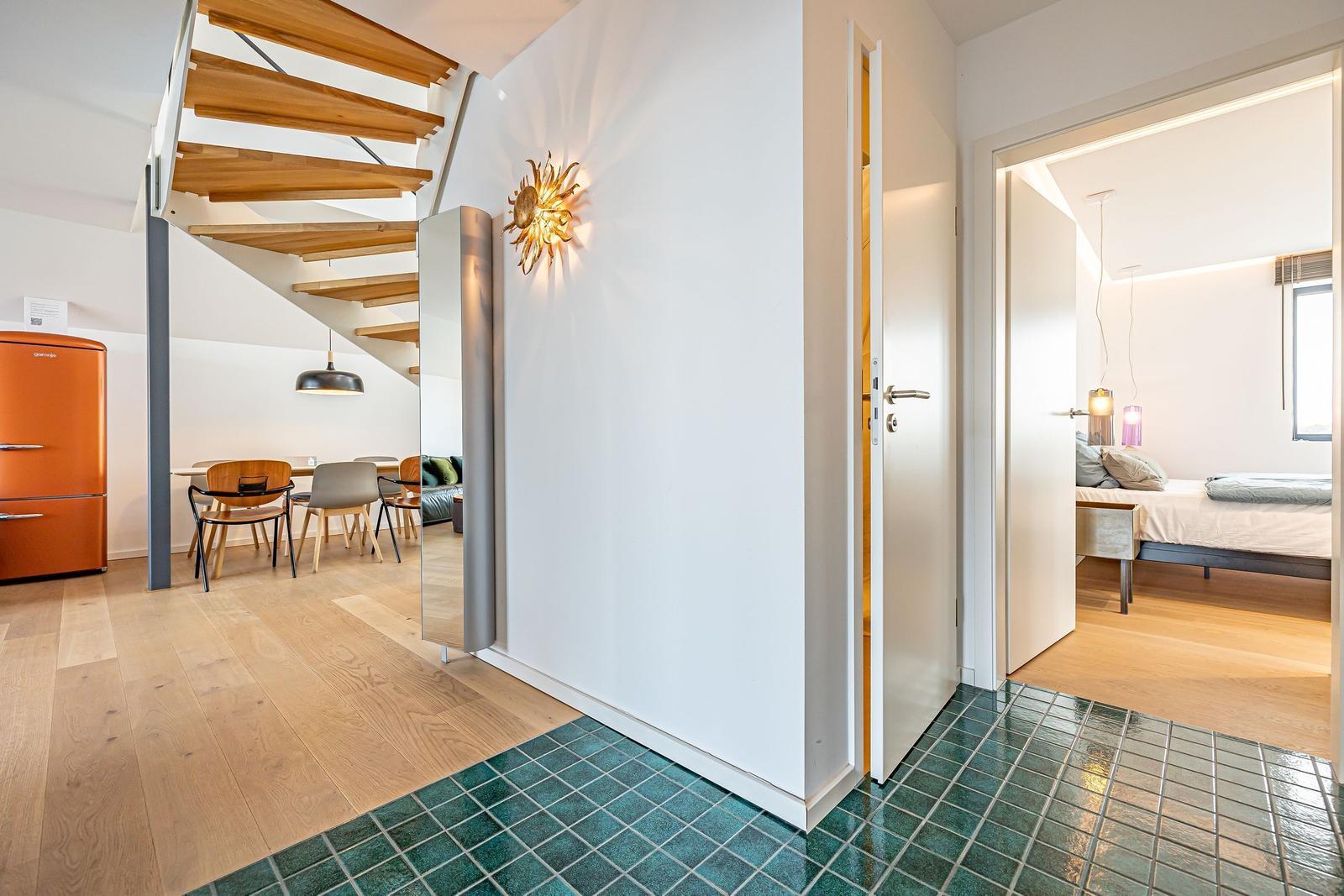 Eingangsbereich mit Holzboden, grünen Fliesen und Blick in Wohn- und Schlafzimmer.