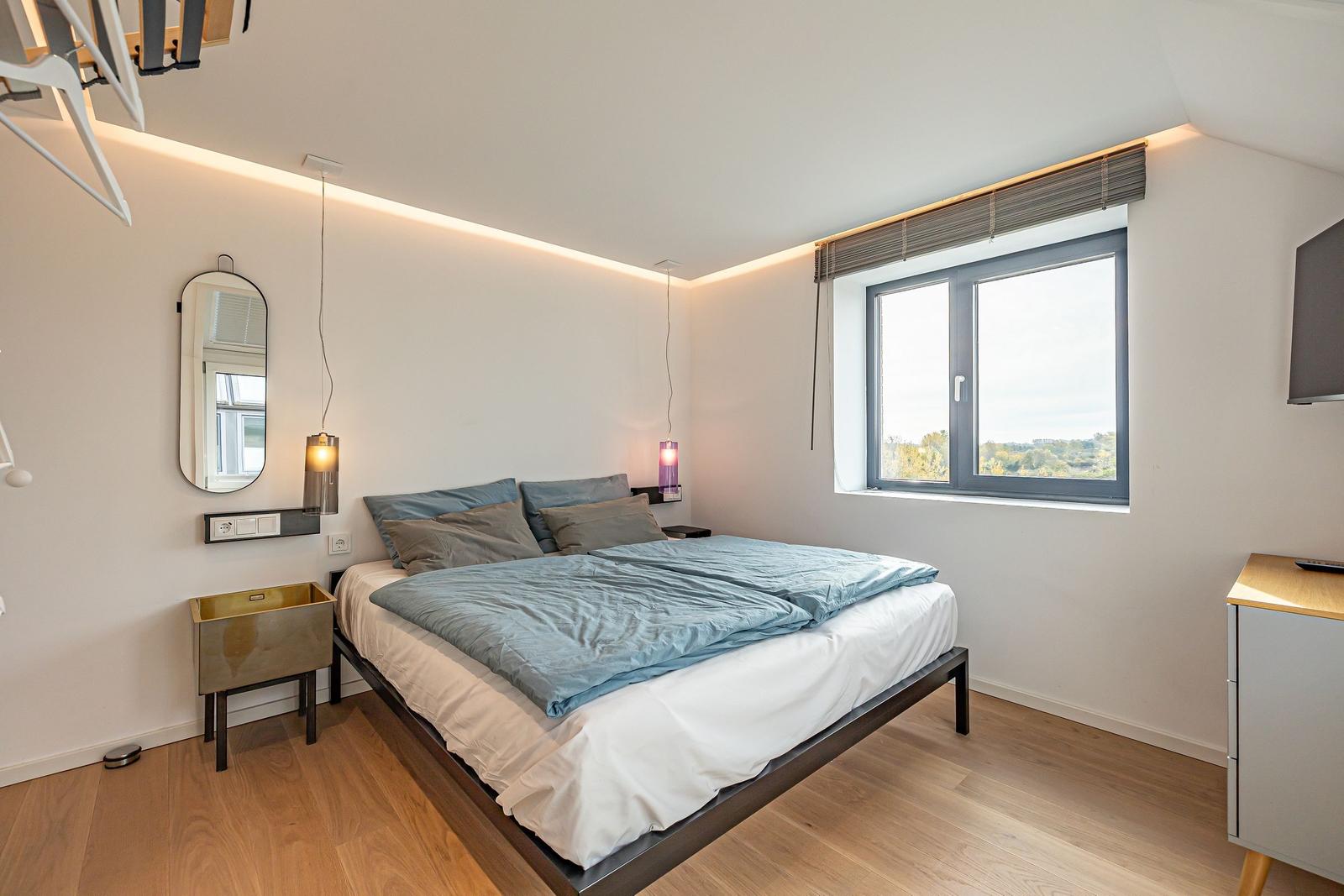 Schlafzimmer mit Bett, Fenster und moderner Beleuchtung.