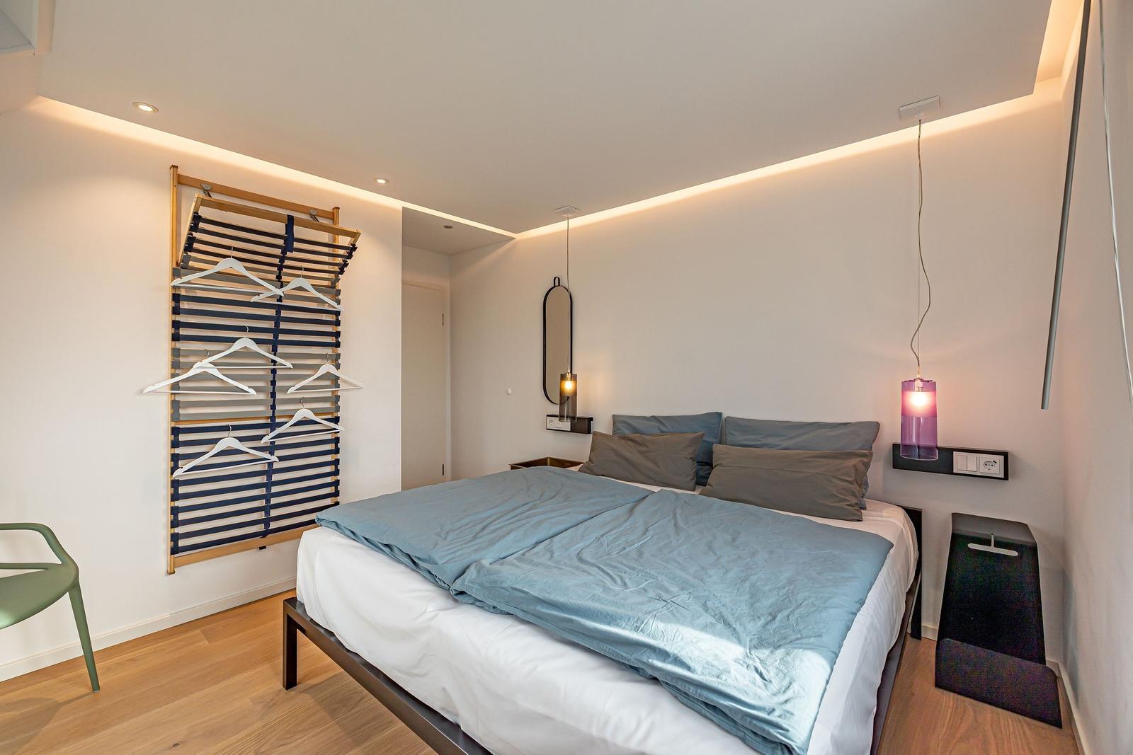 Schlafzimmer mit Bett, Kleiderständer und modernen Lampen.