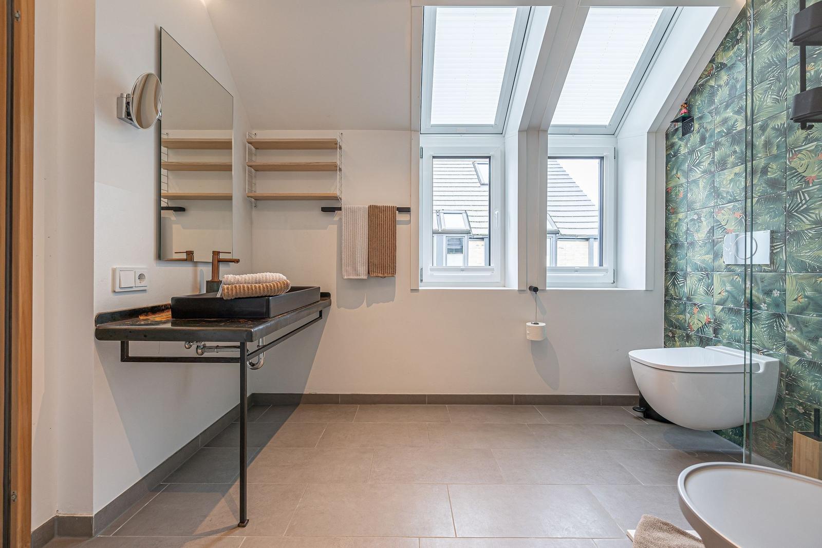 Badezimmer mit Dusche, Toilette und Waschbecken unter Dachfenstern.