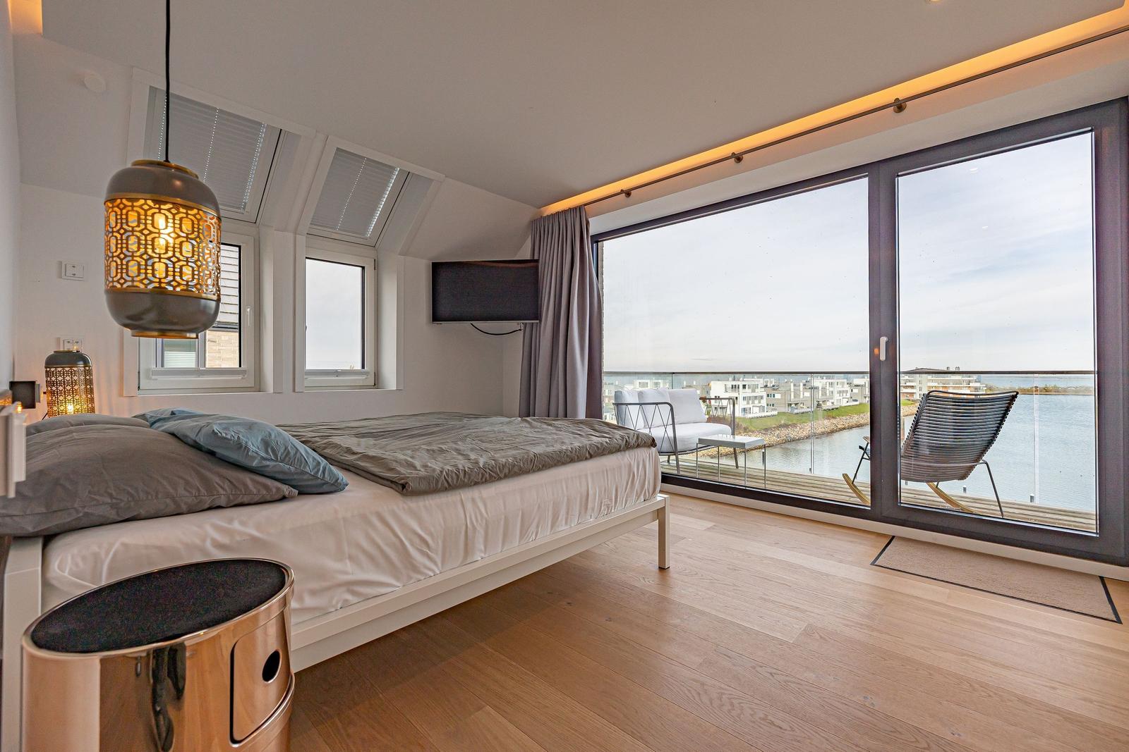 Schlafzimmer mit Balkon und Seeblick. Bett, TV und Holzboden.