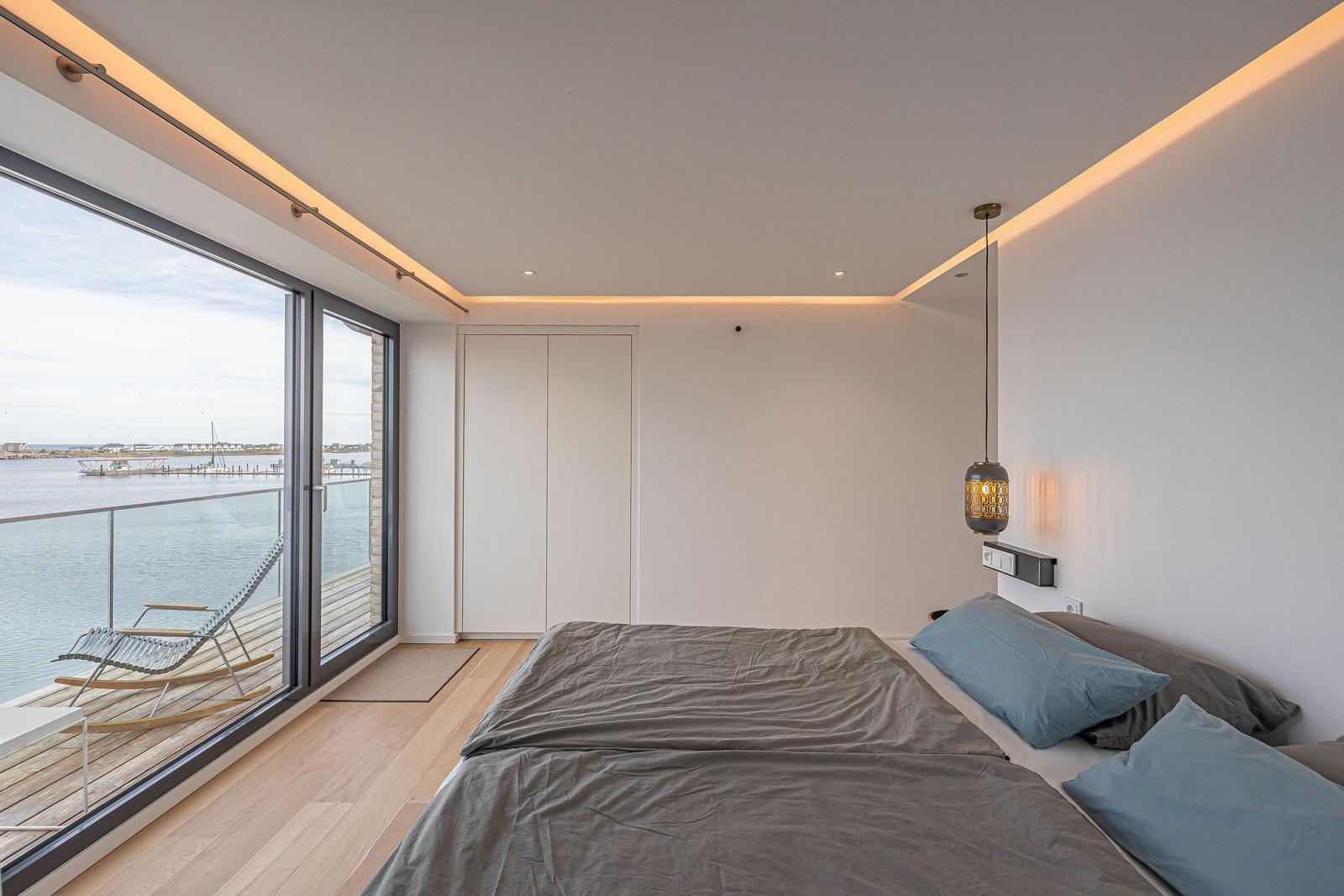 Schlafzimmer mit Blick auf Wasser und Terrasse mit Liege.