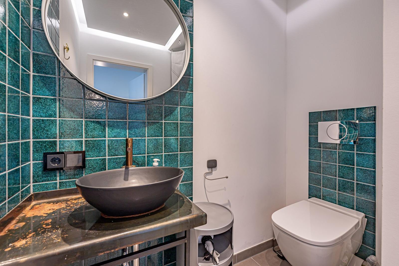 Badezimmer mit Waschbecken, Spiegel und Toilette. Wandfliesen in Türkis.