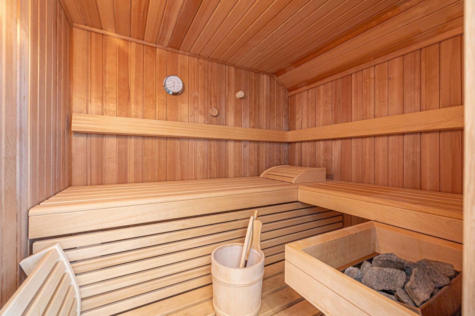 Holzsauna mit Sitzbänken, Steinmulde und Thermometer an der Wand.