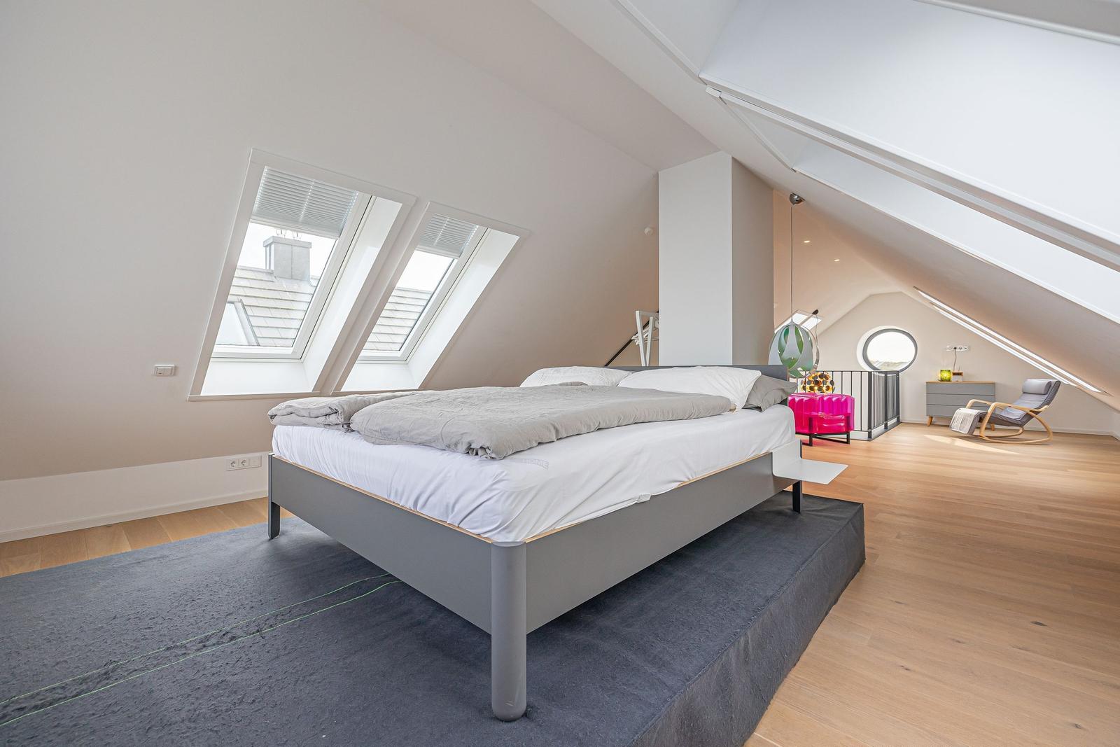 Schlafzimmer mit Dachfenstern, Bett und Sitzgelegenheit.