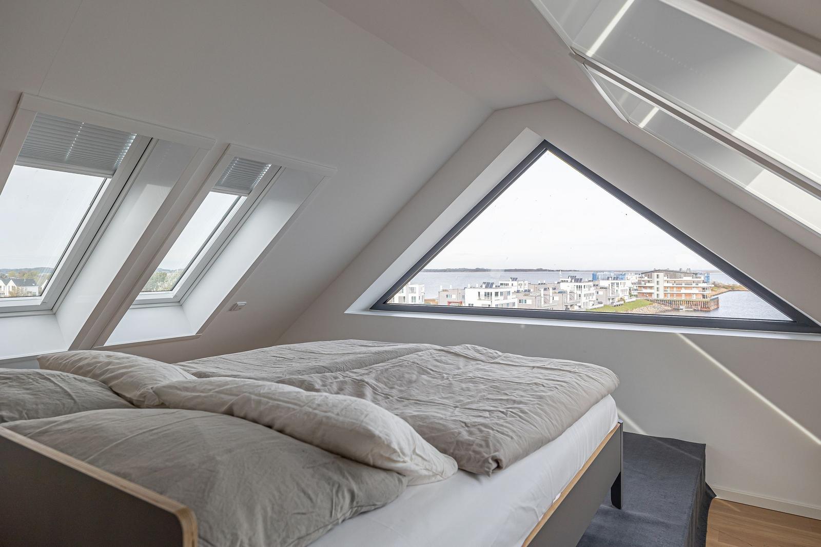 Schlafzimmer mit Dachfenster und Blick auf Wasser und Gebäude.