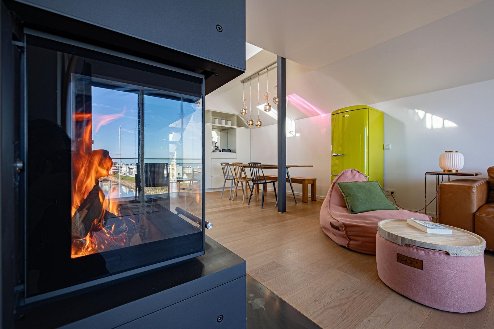 Ein Kamin mit Blick auf Balkon, Wohnbereich mit pinkem Sitzmöbel und gelbem Kühlschrank.