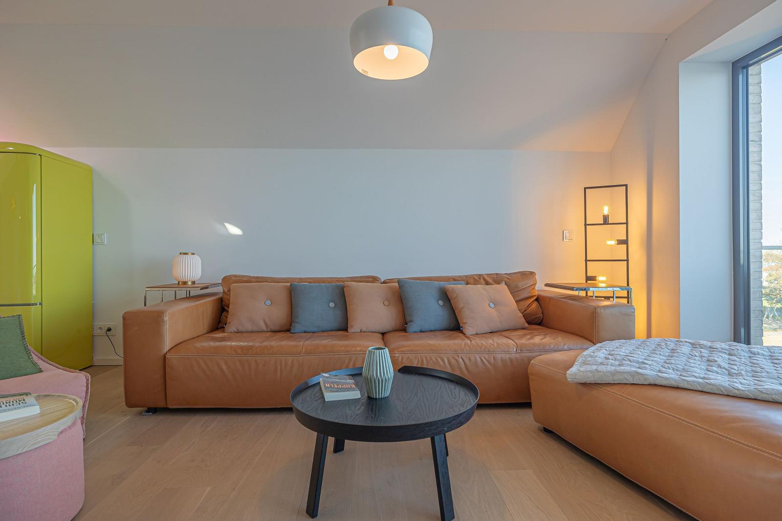 Ein Wohnzimmer mit braunem Ledersofa, runden Tisch und grünem Kühlschrank.