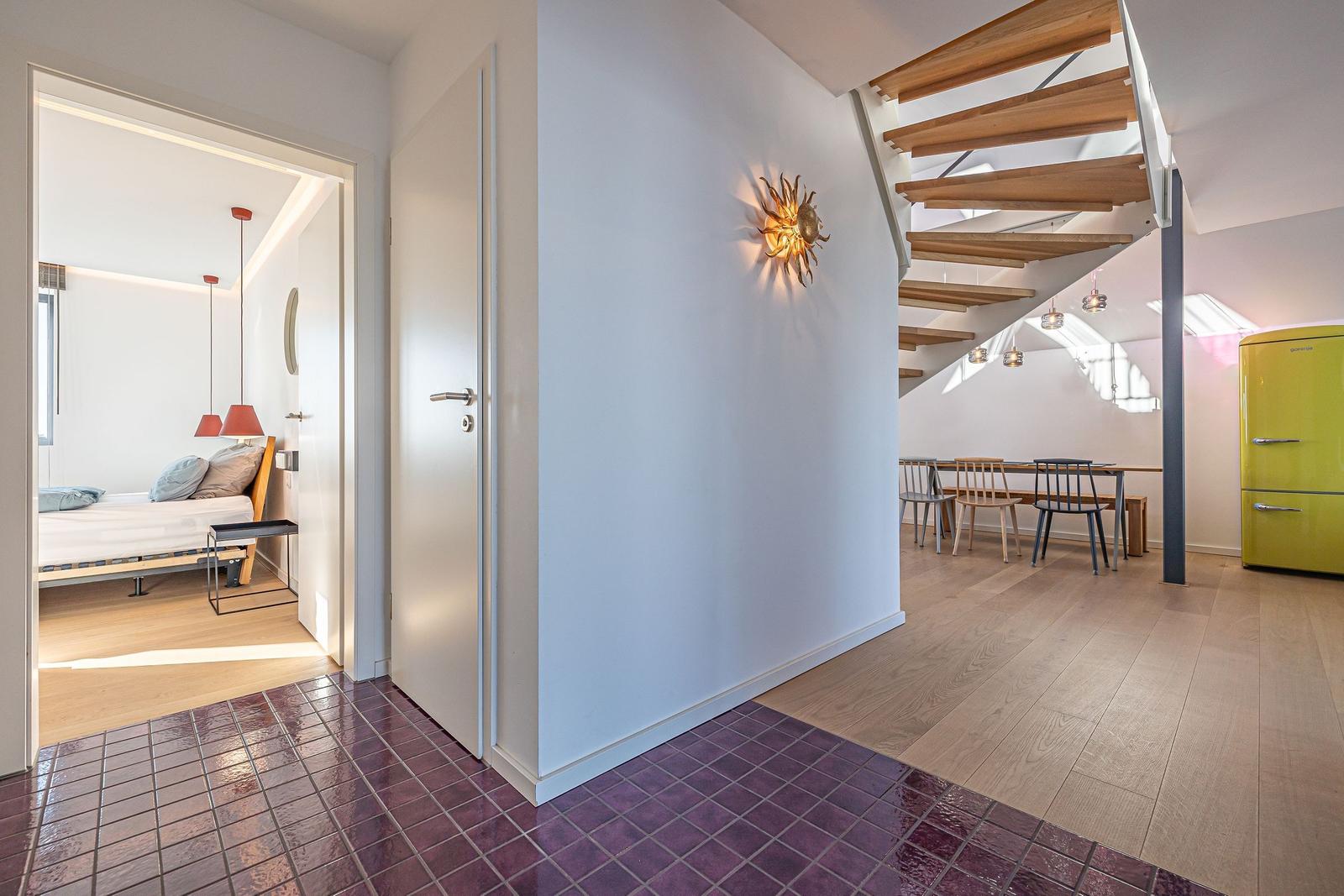 Eingangsbereich mit purpurfarbenen Fliesen, Treppe und Sicht auf Schlafzimmer und Essbereich.