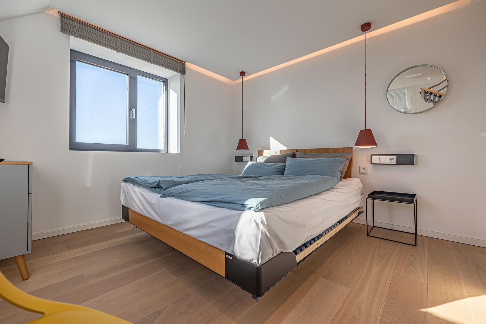 Schlafzimmer mit Doppelbett, Fenster und moderner Beleuchtung.