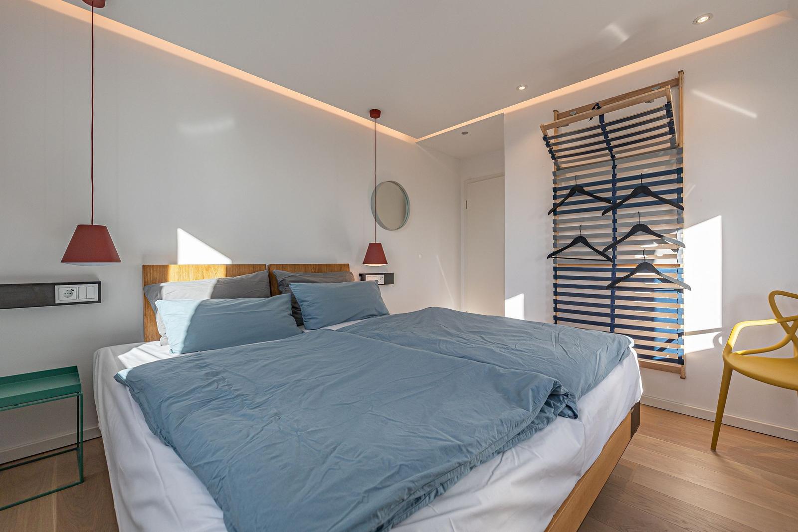 Schlafzimmer mit Bett, Kleiderständer und Stuhl.