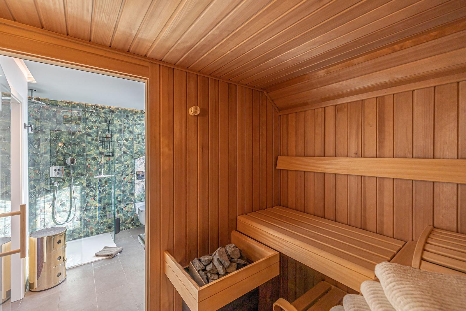 Sauna mit Holzbank und Steinmulde. Durchgang zur Dusche mit tropischen Fliesen.