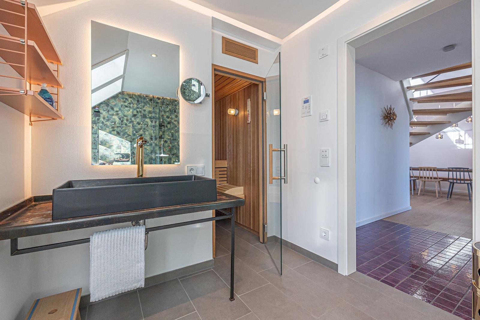 Bad mit Waschbecken, Spiegel und Sauna. Durchgang zu Wohnbereich mit Treppe.