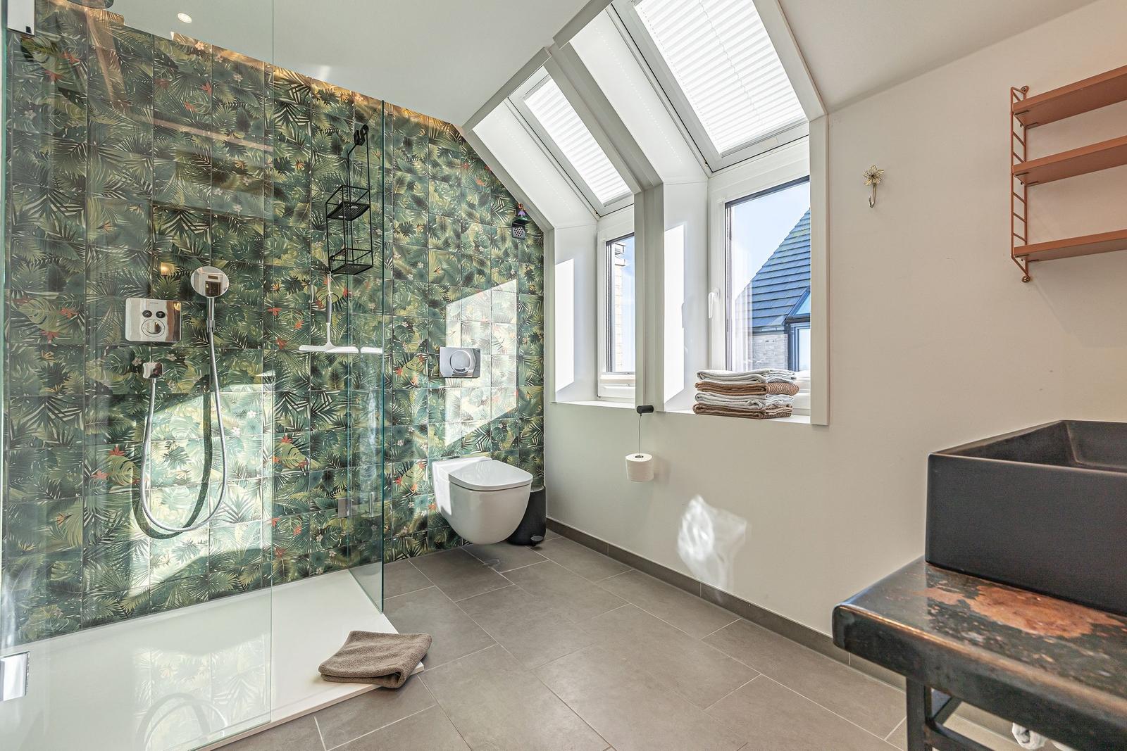 Badezimmer mit Dusche, Toilette und Waschtisch unter Dachfenstern.