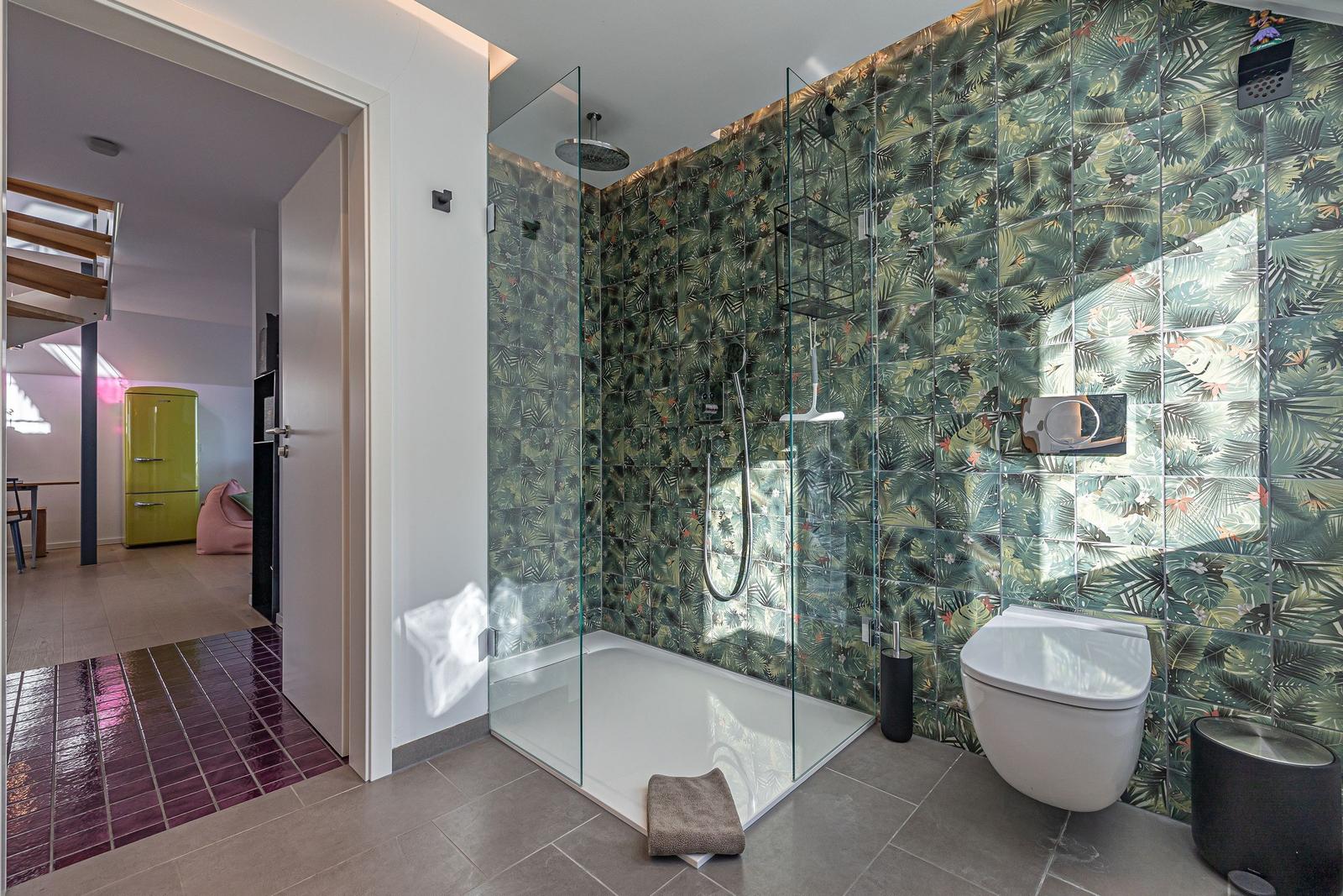 Badezimmer mit Dusche und Toilette, Wandfliesen mit tropischem Motiv.