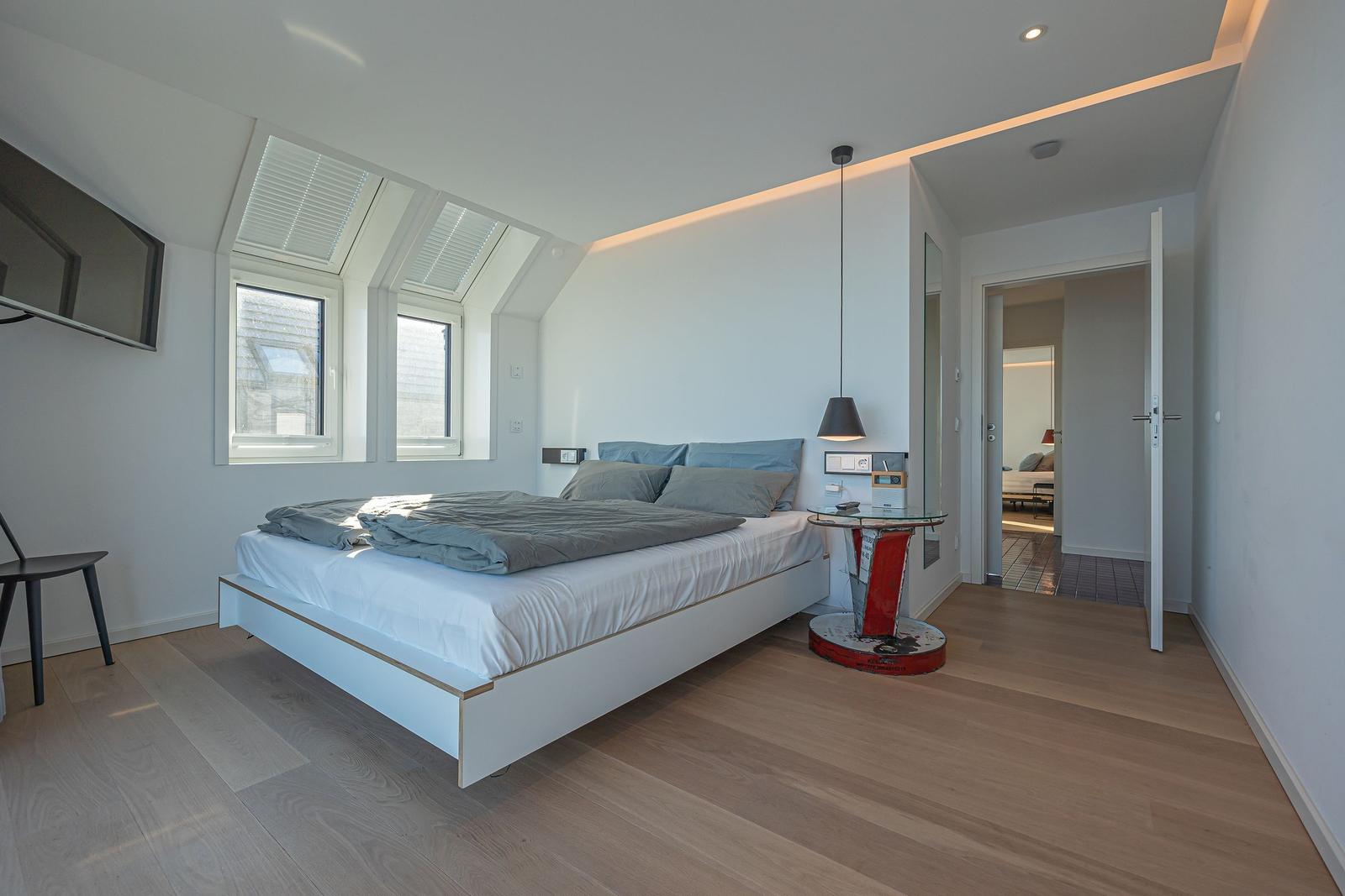 Schlafzimmer mit Dachfenstern, Bett und Tisch.