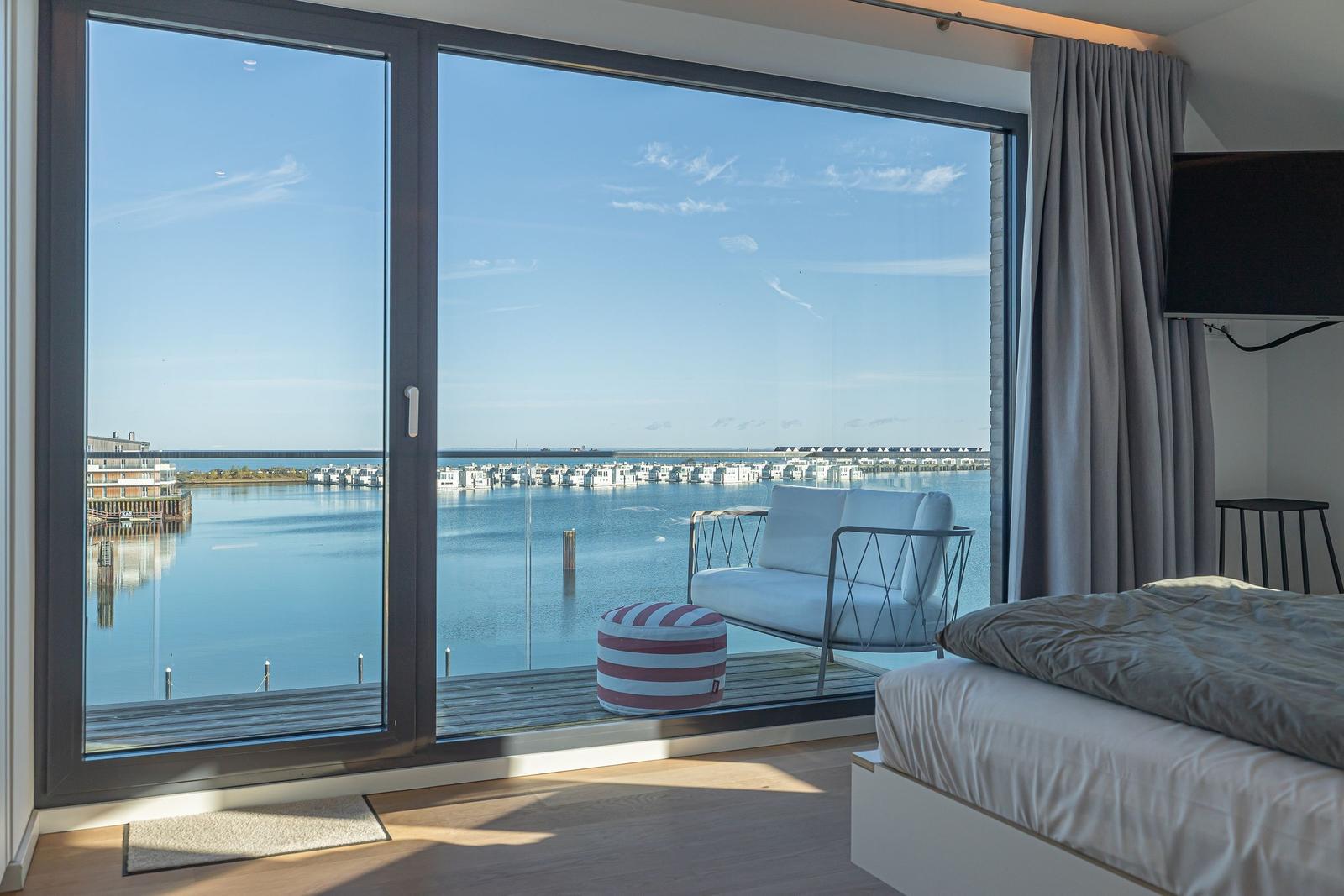 Schlafzimmer mit Blick auf Wasser und Hafen. Balkon mit Sitzmöbeln und Bett.
