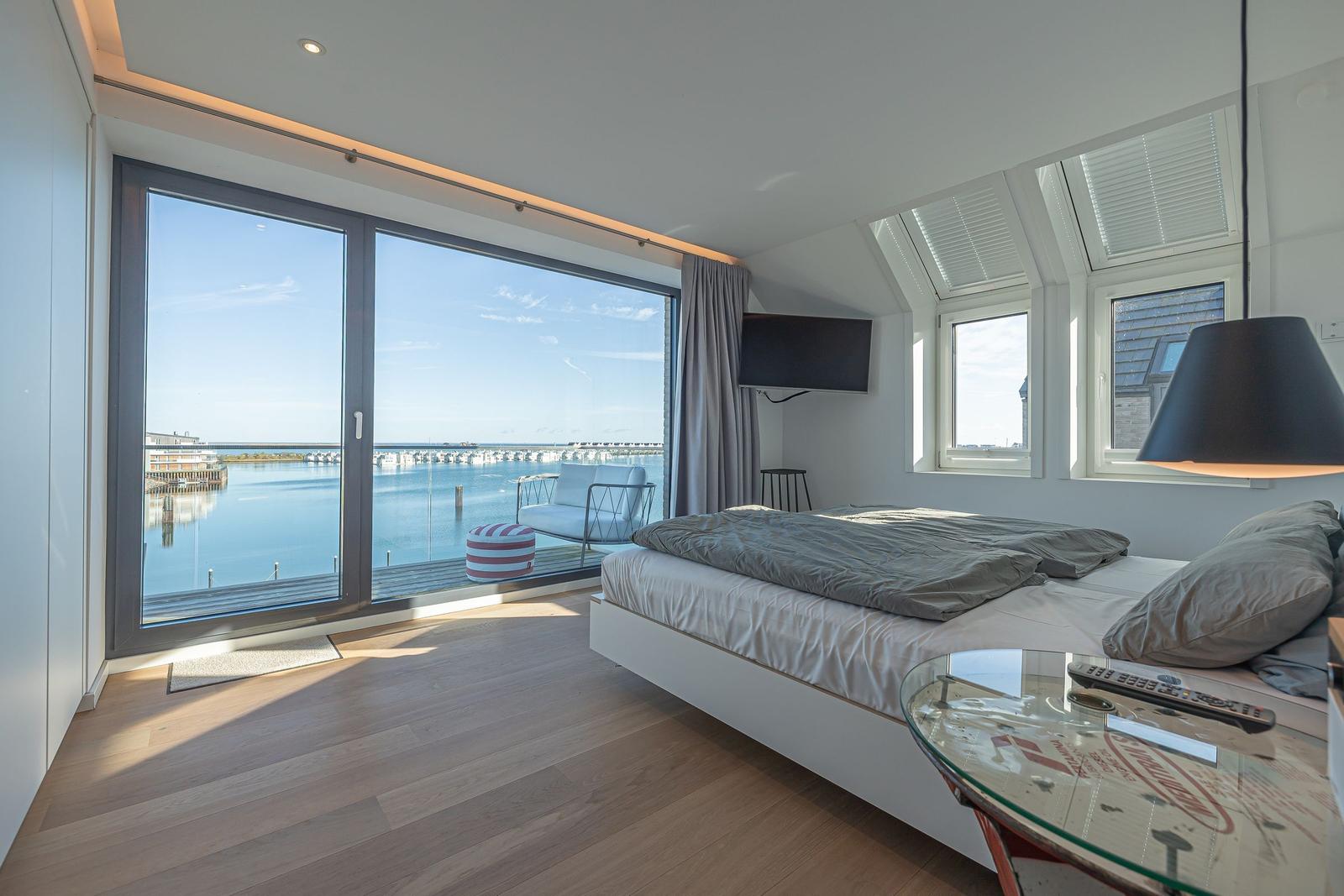 Schlafzimmer mit Blick auf Hafen und Booten. Bett, TV und Glas-Tisch.