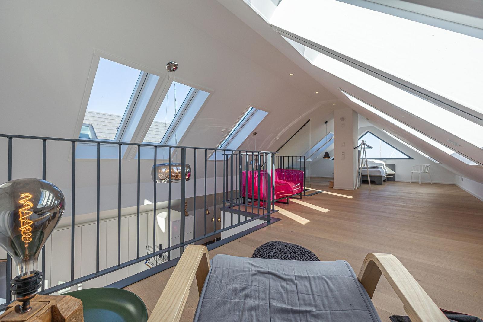 Dachgeschoss mit Holzboden, Dachfenstern und pinkem Sofa.